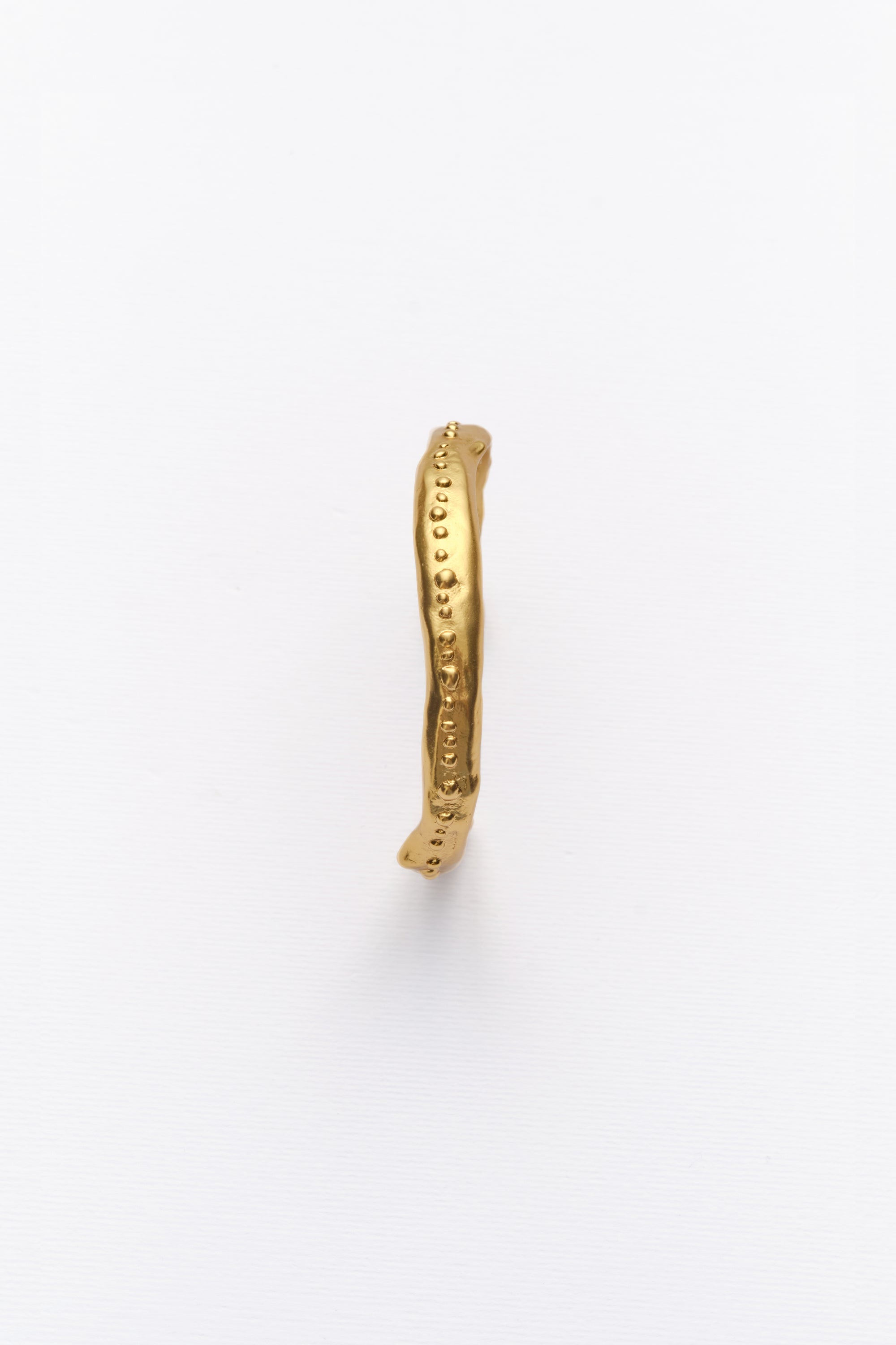 Minimalist textured gold bangle bracelet with organic hammered finish on white background