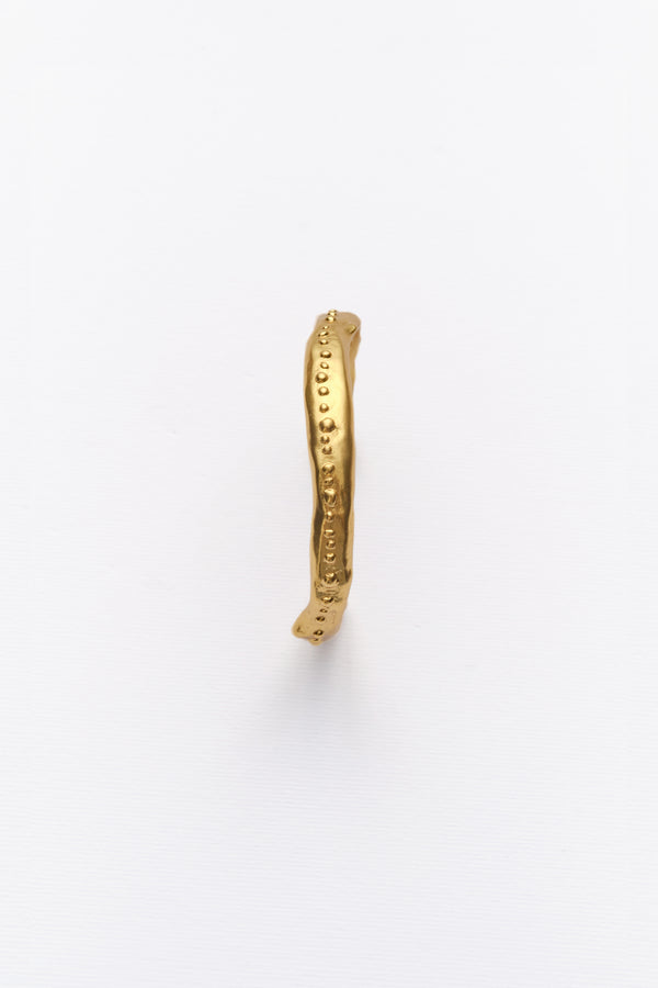Minimalist textured gold bangle bracelet with organic hammered finish on white background