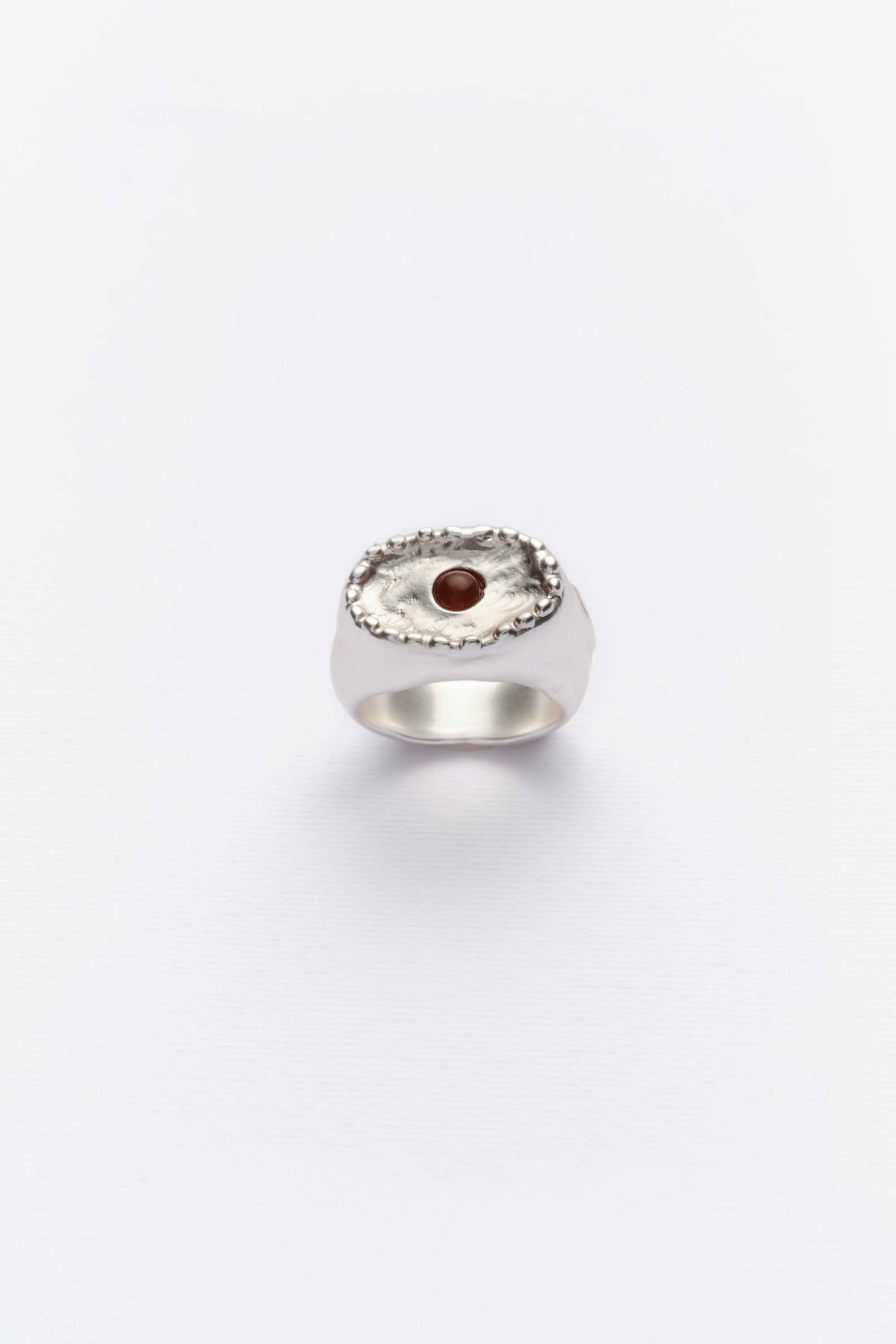A vintage-style silver ring with a central red cabochon and intricate detailing around the edge.