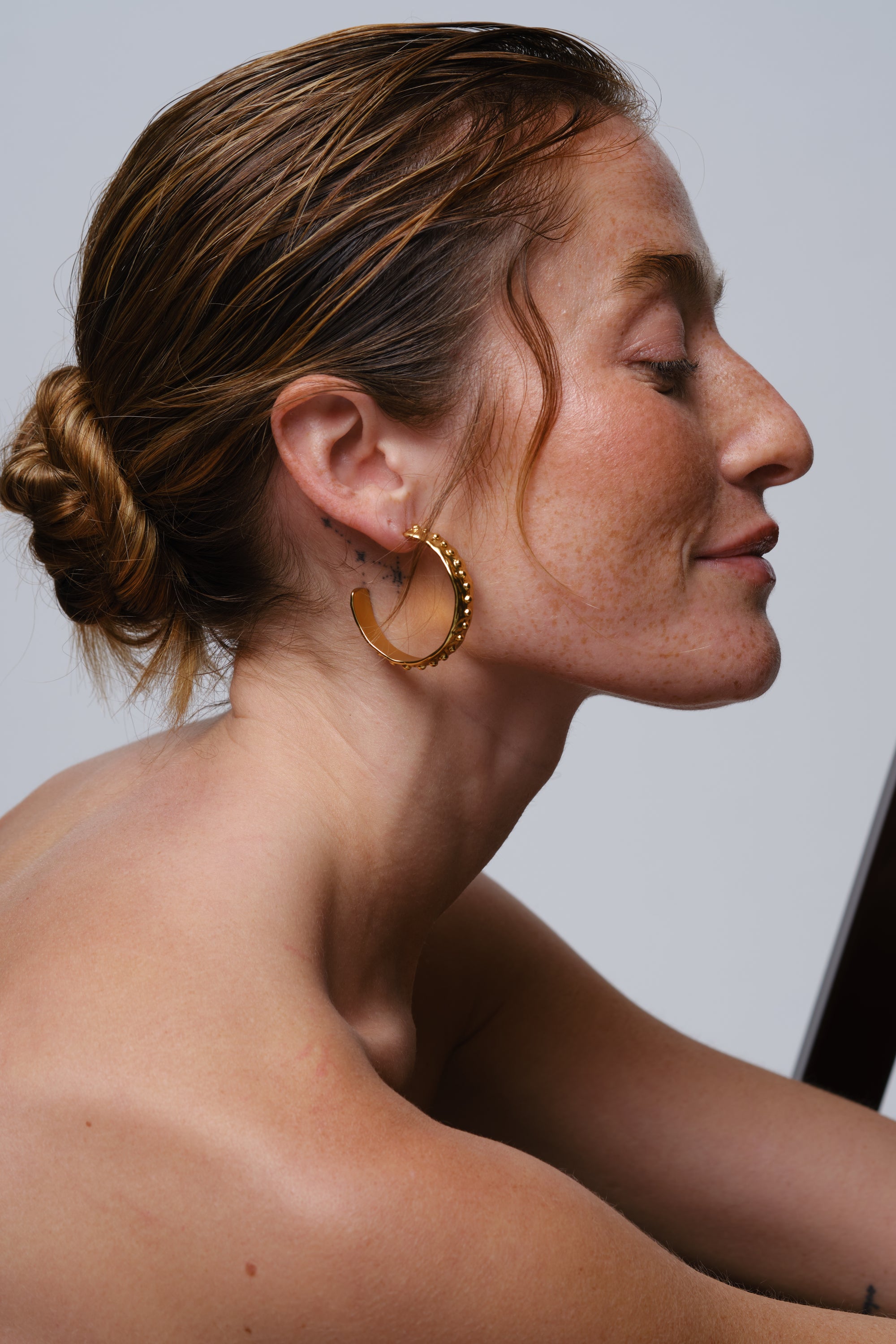 Close-up side profile of woman wearing gold textured hoop earrings with hair styled in a bun