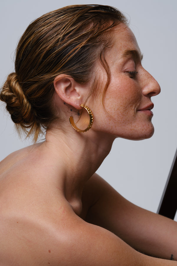 Close-up side profile of woman wearing gold textured hoop earrings with hair styled in a bun