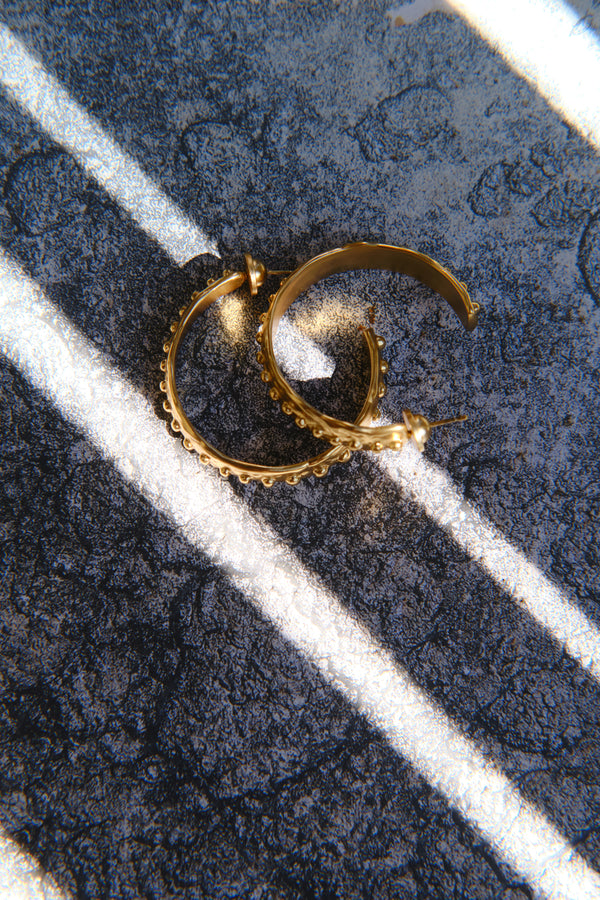 Gold textured hoop earrings styled on stone surface with light shadow