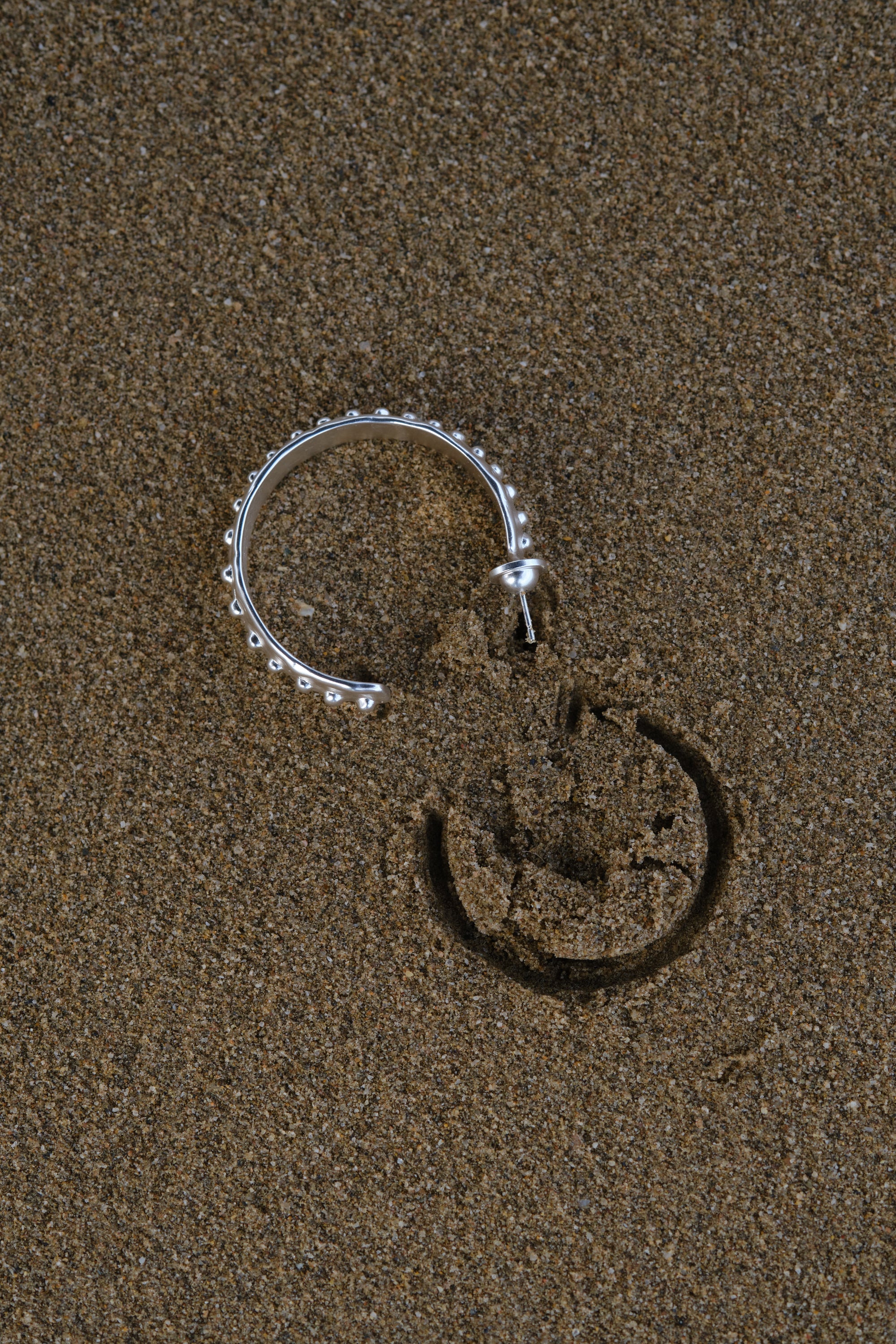 Silver textured hoop earring with beaded edge on sand background