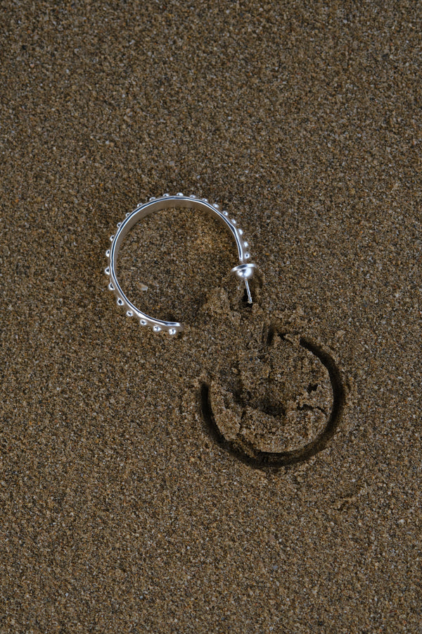 Silver textured hoop earring with beaded edge on sand background