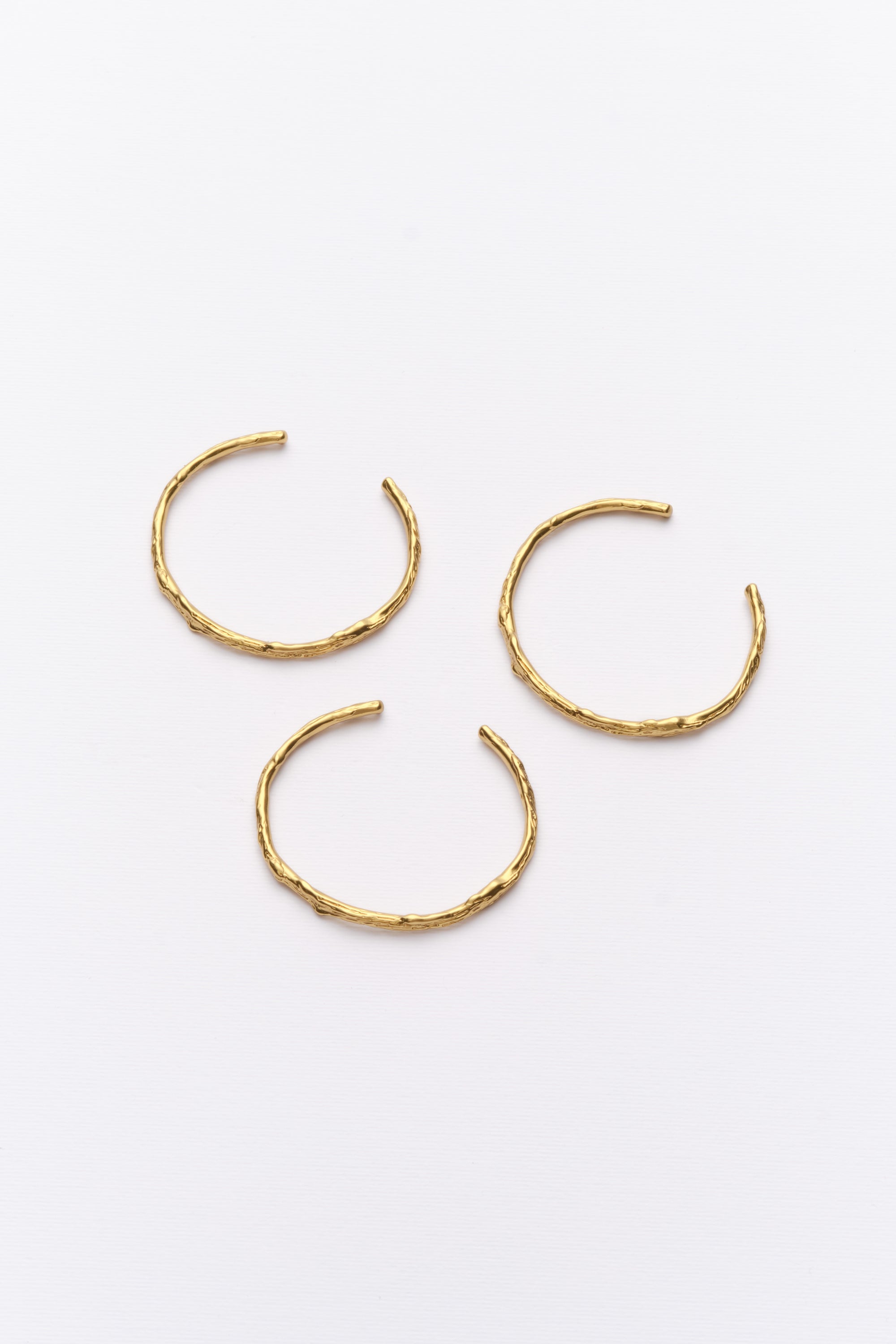 A set of three gold-colored cuff bracelets with a hoop design, displayed against a white background.