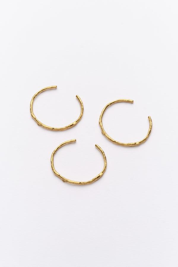A set of three gold-colored cuff bracelets with a hoop design, displayed against a white background.