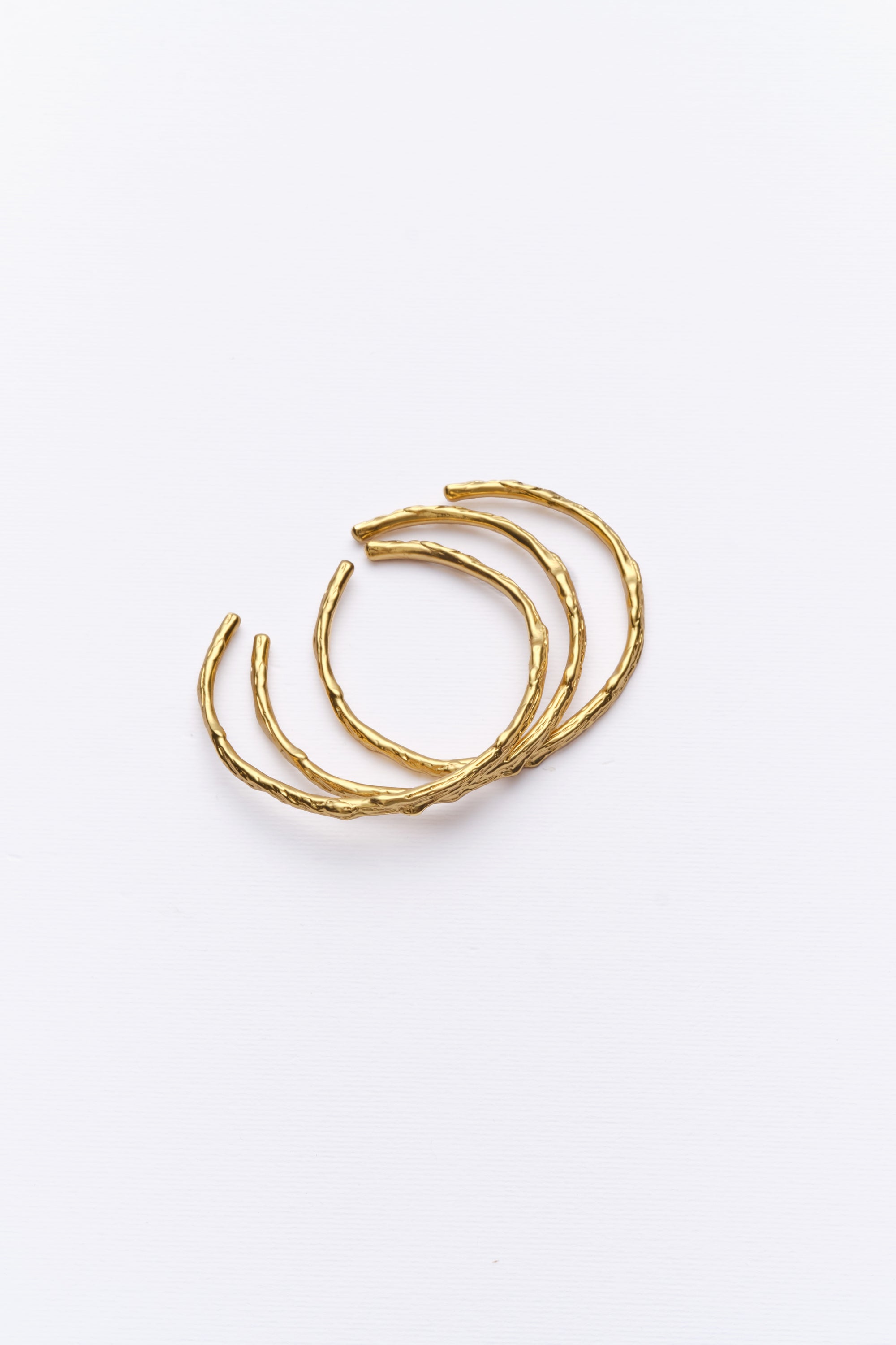 A set of three gold-colored cuff bracelets with a hoop design, displayed against a white background.