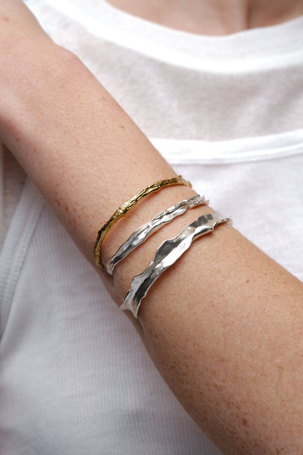 Mixed gold and silver textured cuff bracelets worn on model