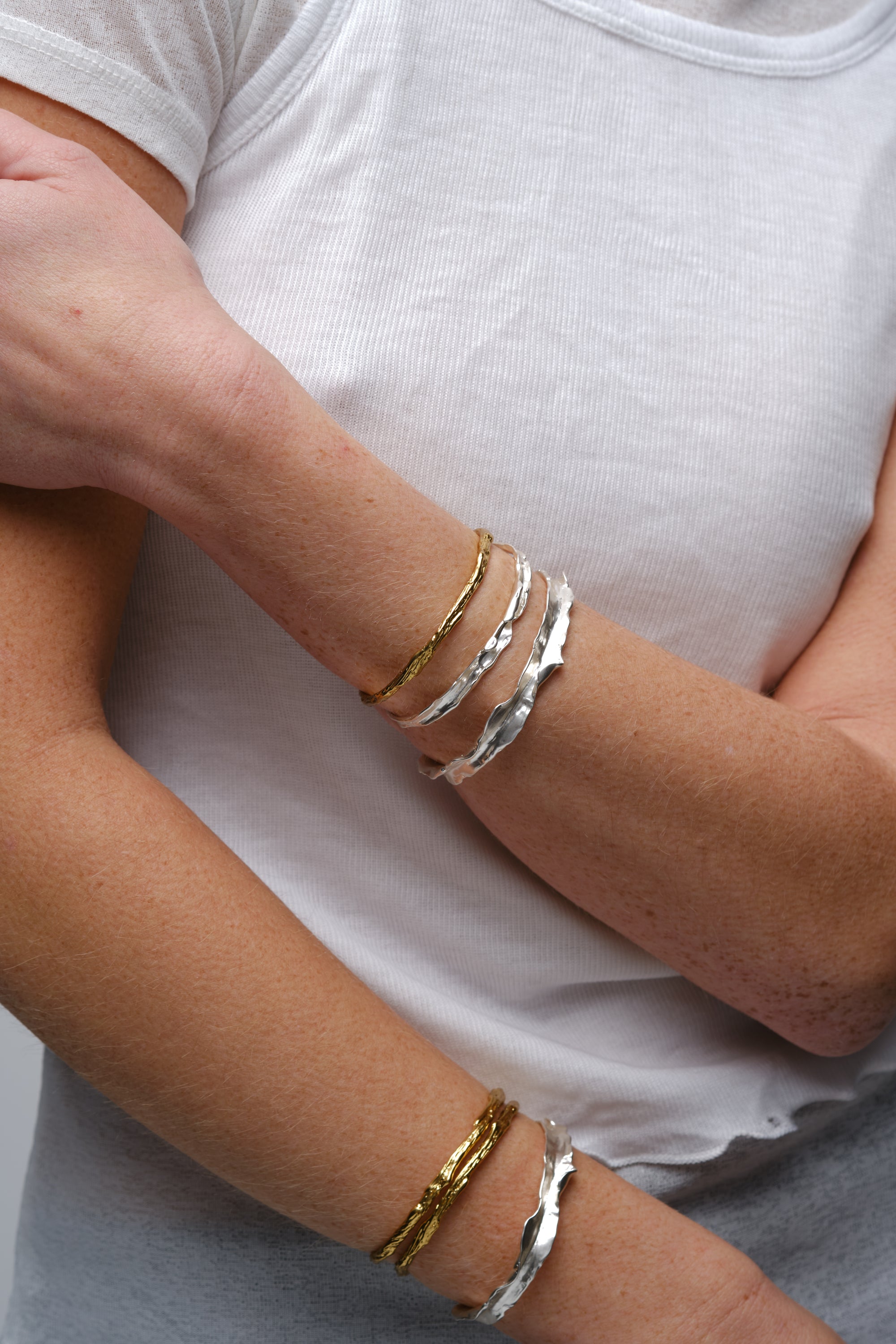Stacked textured cuff bracelets in gold and silver worn on model