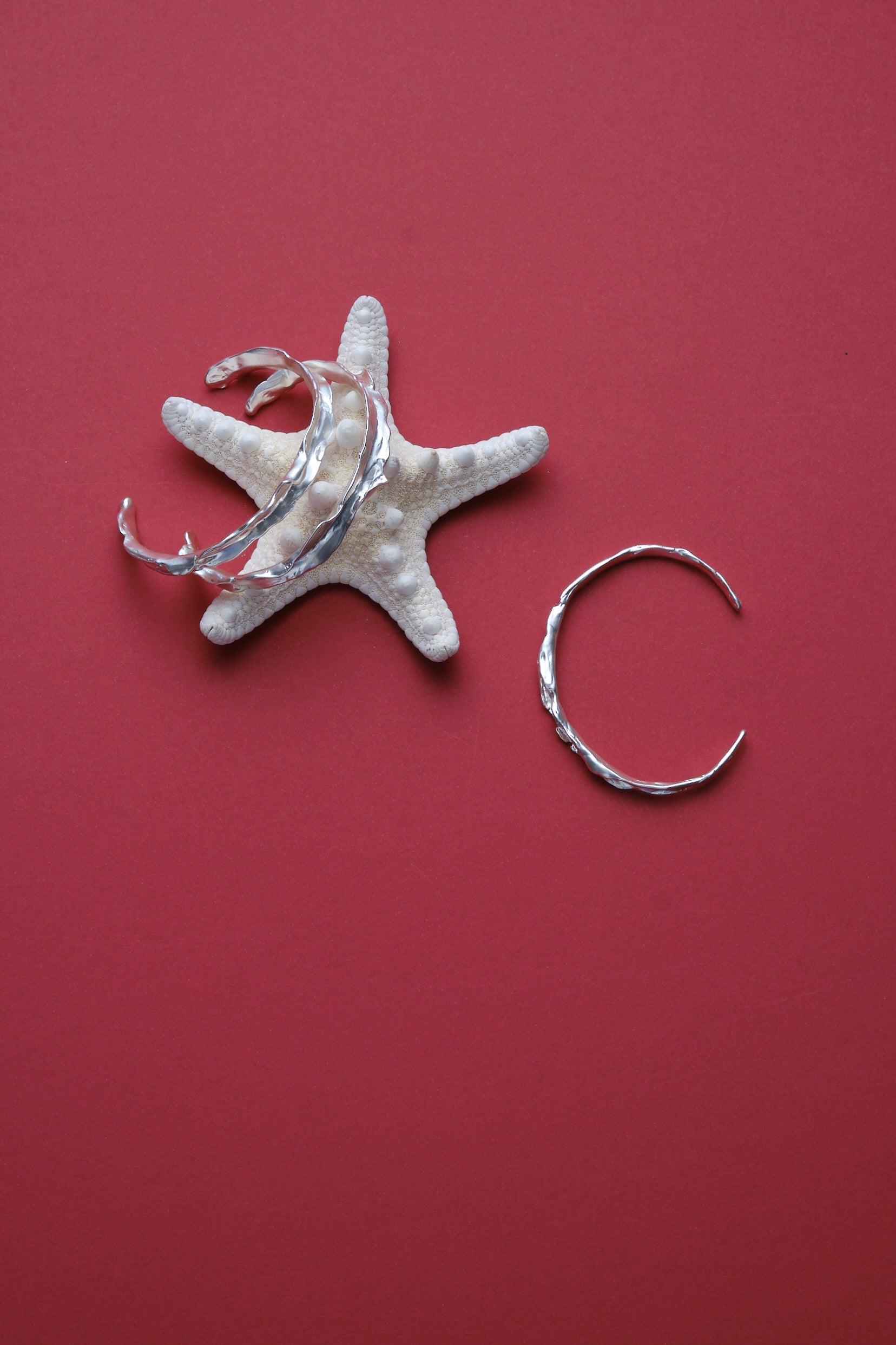 Set of sculptural textured silver bangles styled with starfish on red background