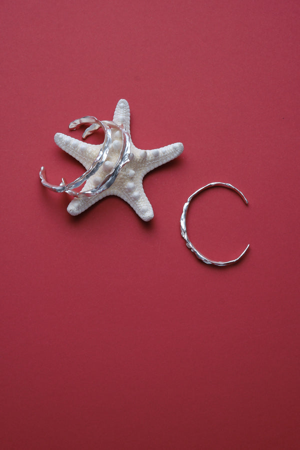 Set of sculptural textured silver bangles styled with starfish on red background
