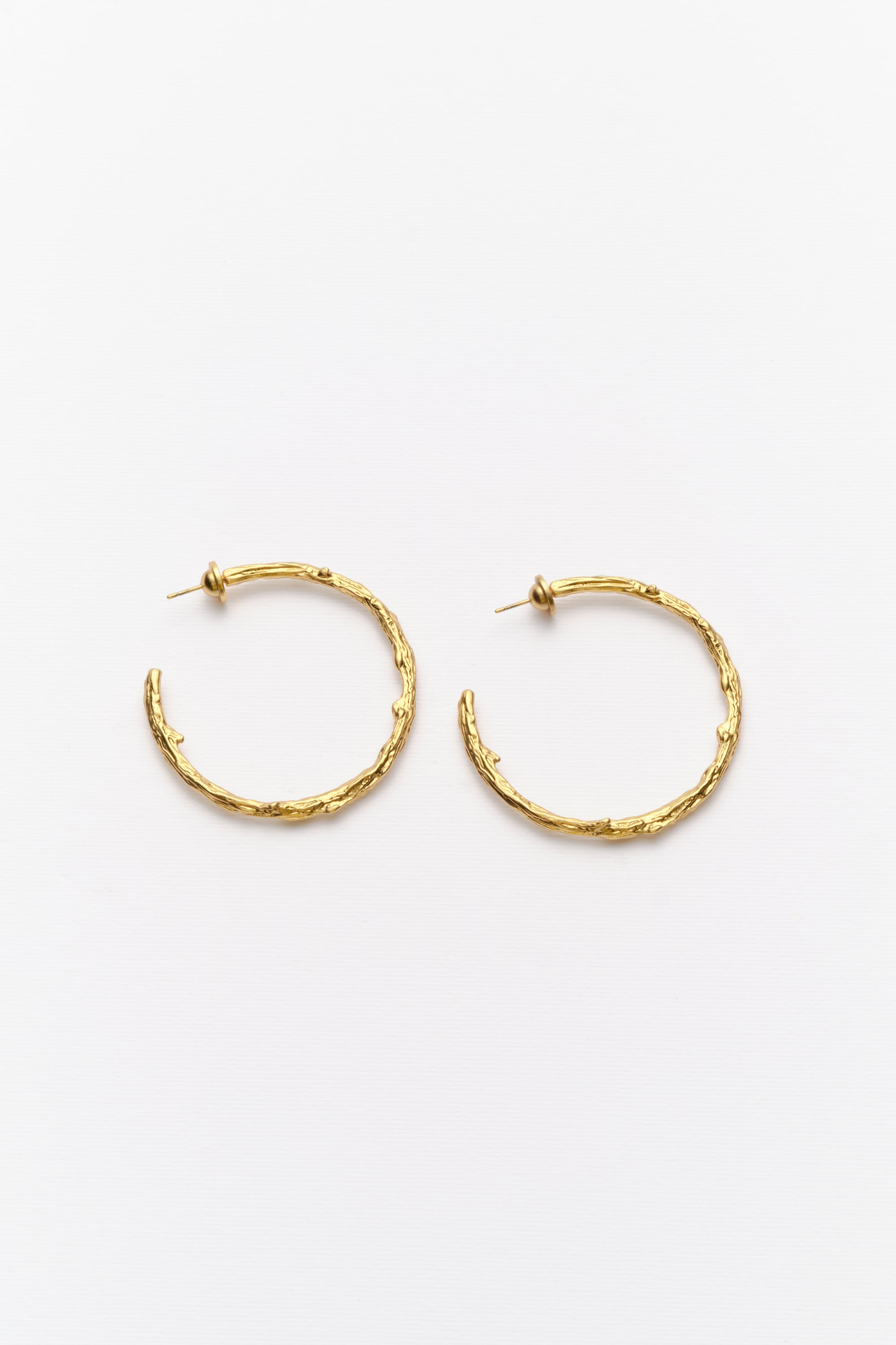 A pair of gold-colored hoop earrings with an organic texture, displayed against a white background