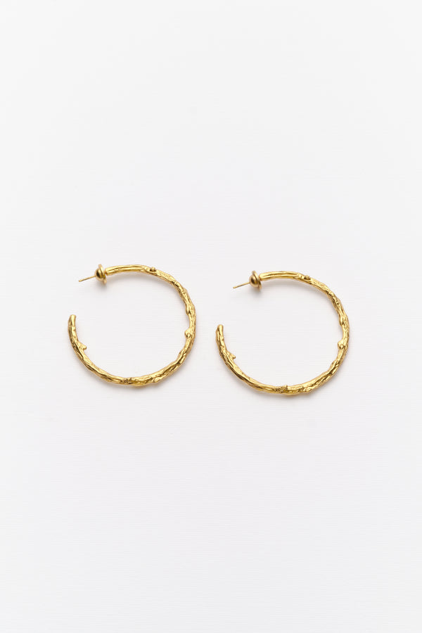 A pair of gold-colored hoop earrings with an organic texture, displayed against a white background
