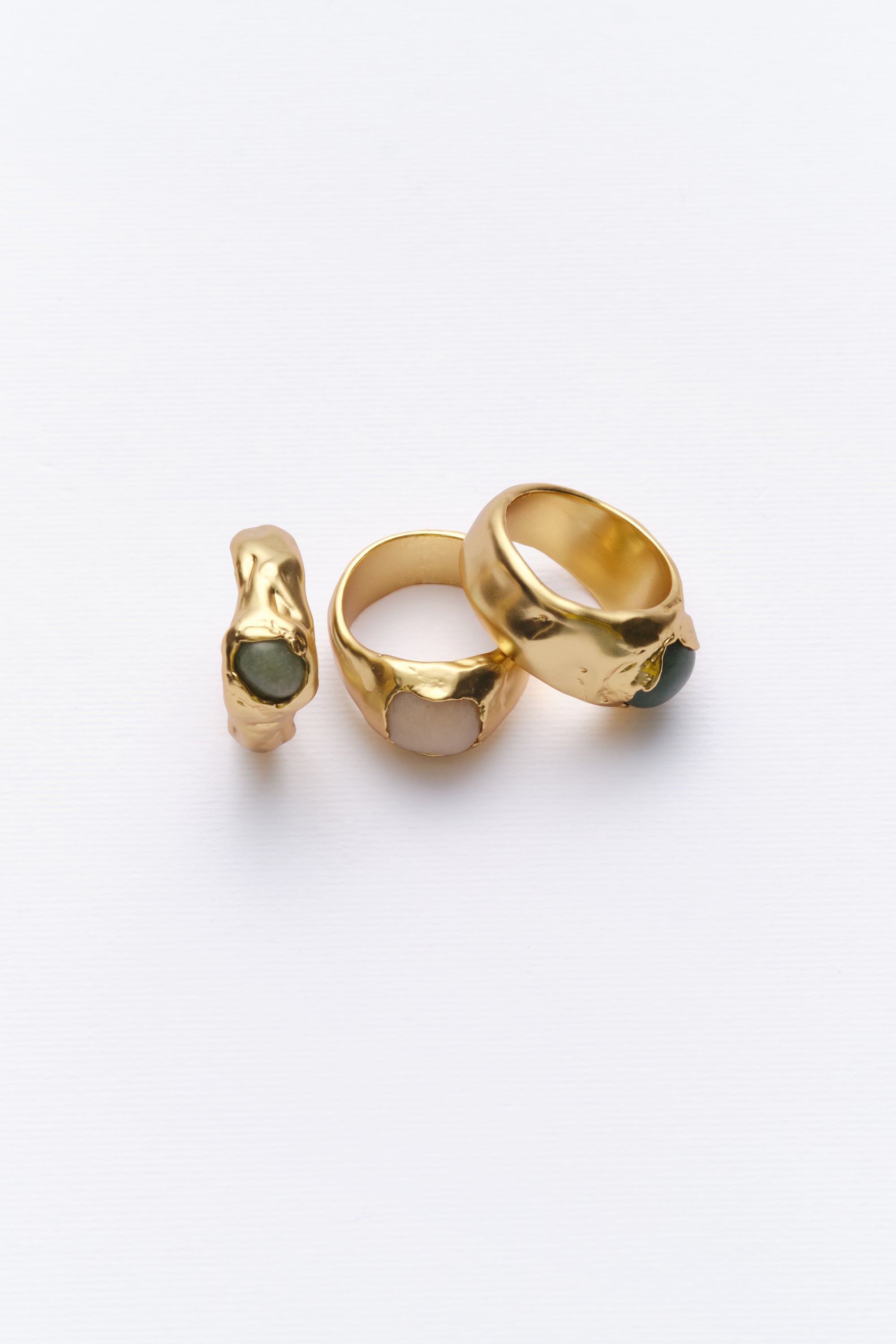 Angled view of gold organic signet rings with green and white gemstones