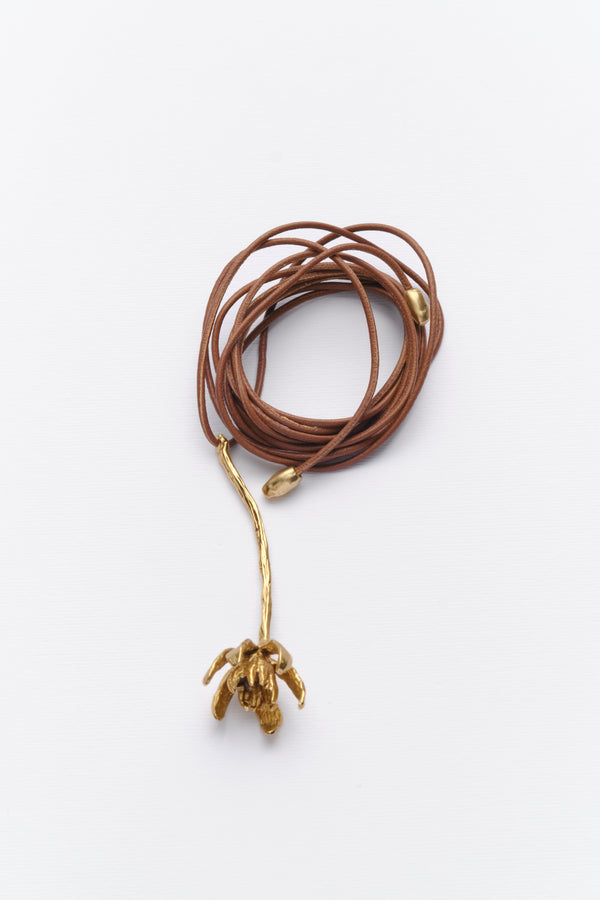 A long necklace with a leather cord and a gold-colored metal pendant shaped like an iris.