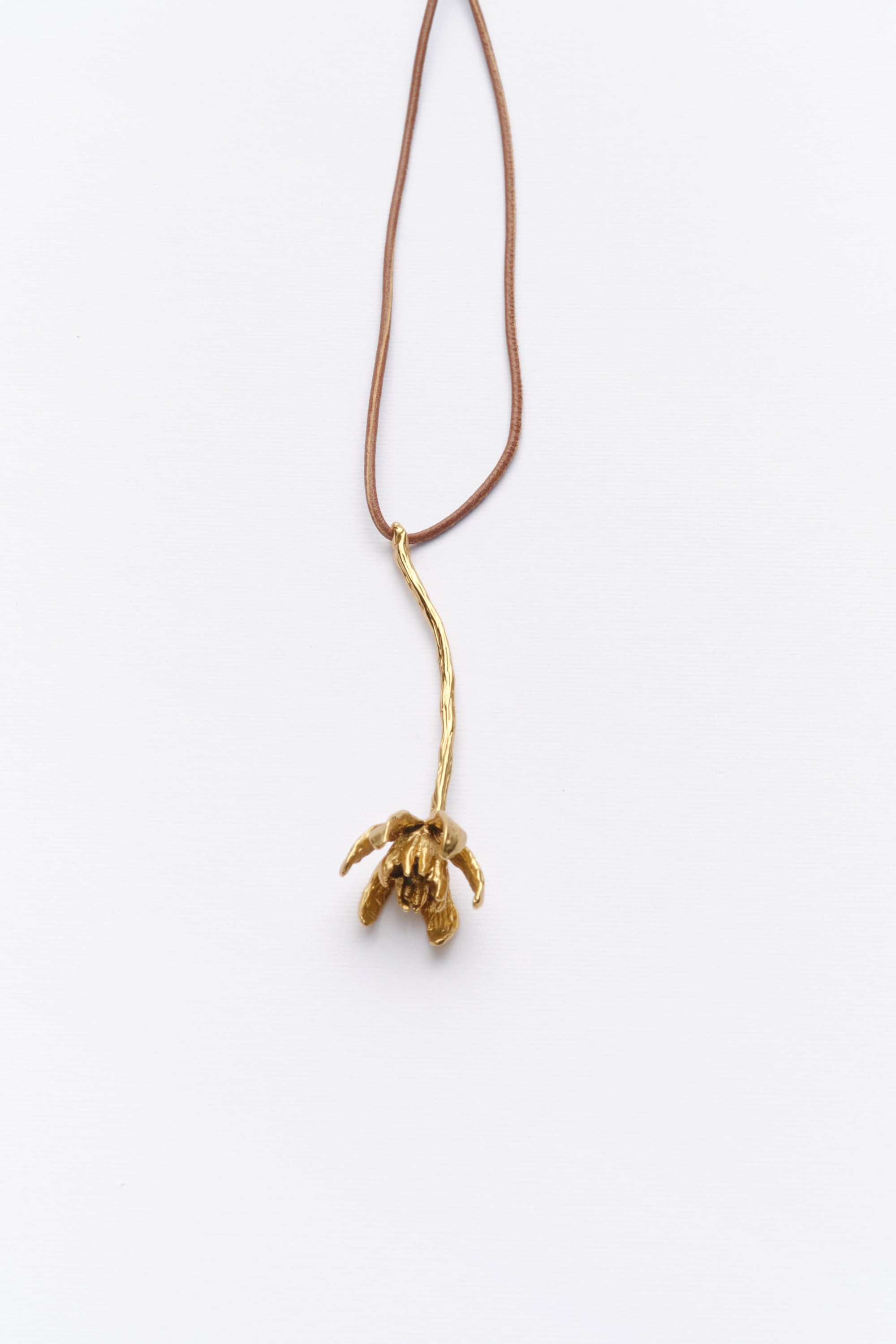 A long necklace with a leather cord and a gold-colored metal pendant shaped like an iris.