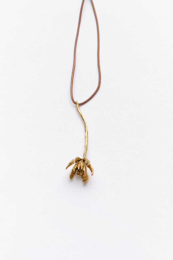 A long necklace with a leather cord and a gold-colored metal pendant shaped like an iris.