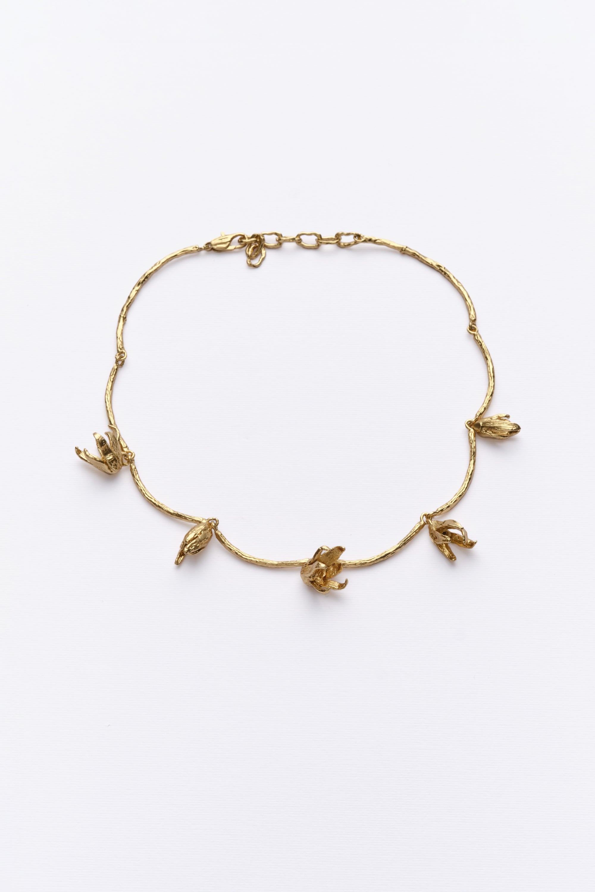 A gold-colored necklace with a series of metal shapes resembling irises Blooming across the collarbone.