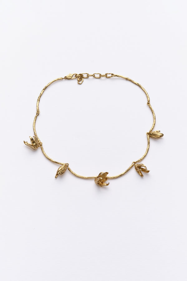 A gold-colored necklace with a series of metal shapes resembling irises Blooming across the collarbone.