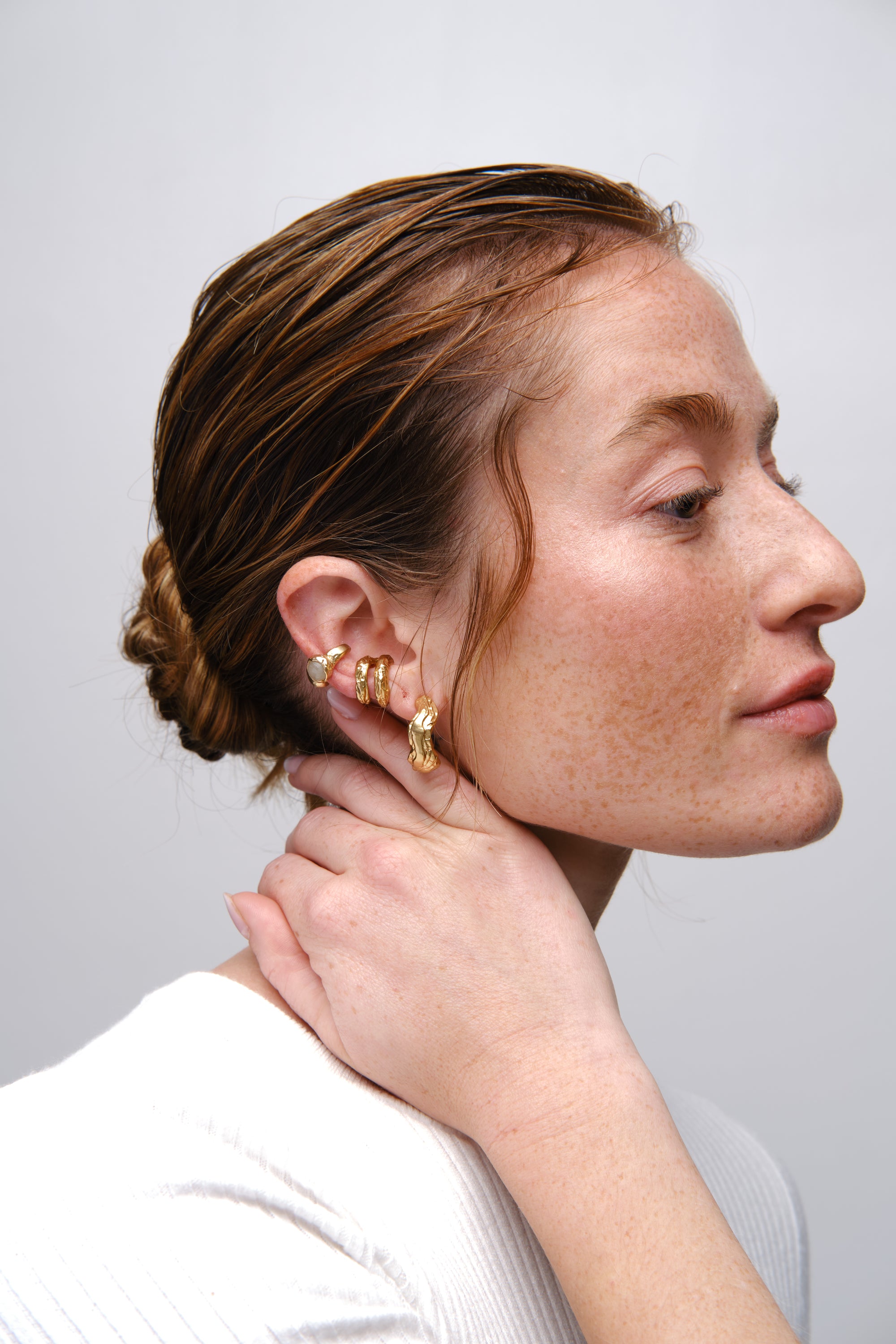 Model wearing gold ear cuff and sculptural hoop earrings side portrait