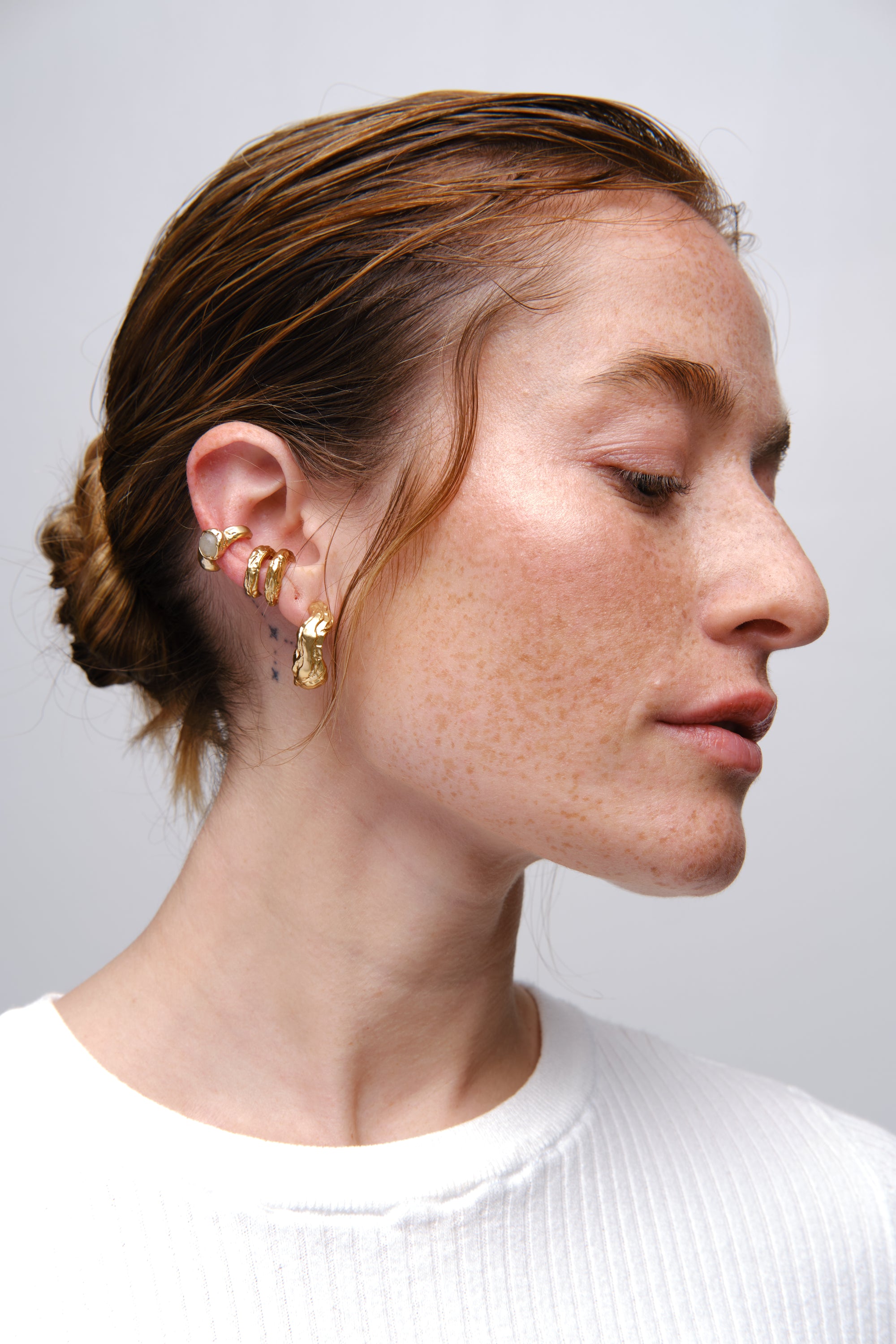 Gold sculptural ear stack earrings worn on model profile close-up