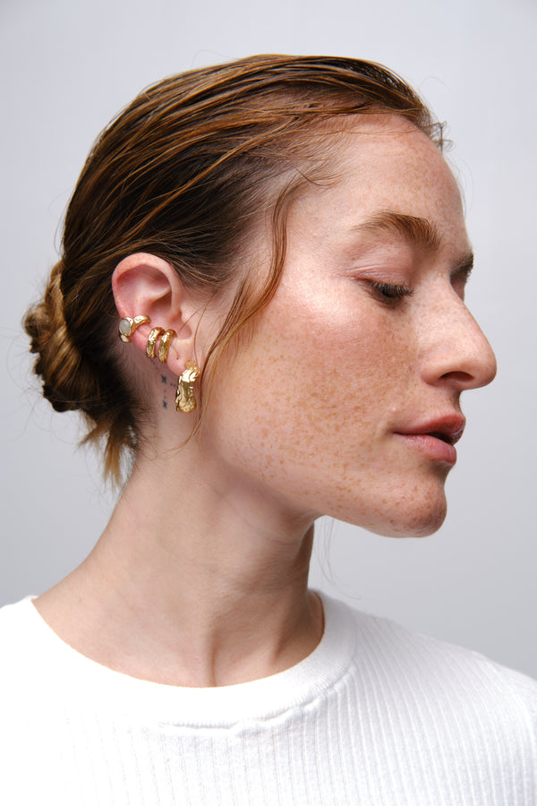 Gold sculptural ear stack earrings worn on model profile close-up