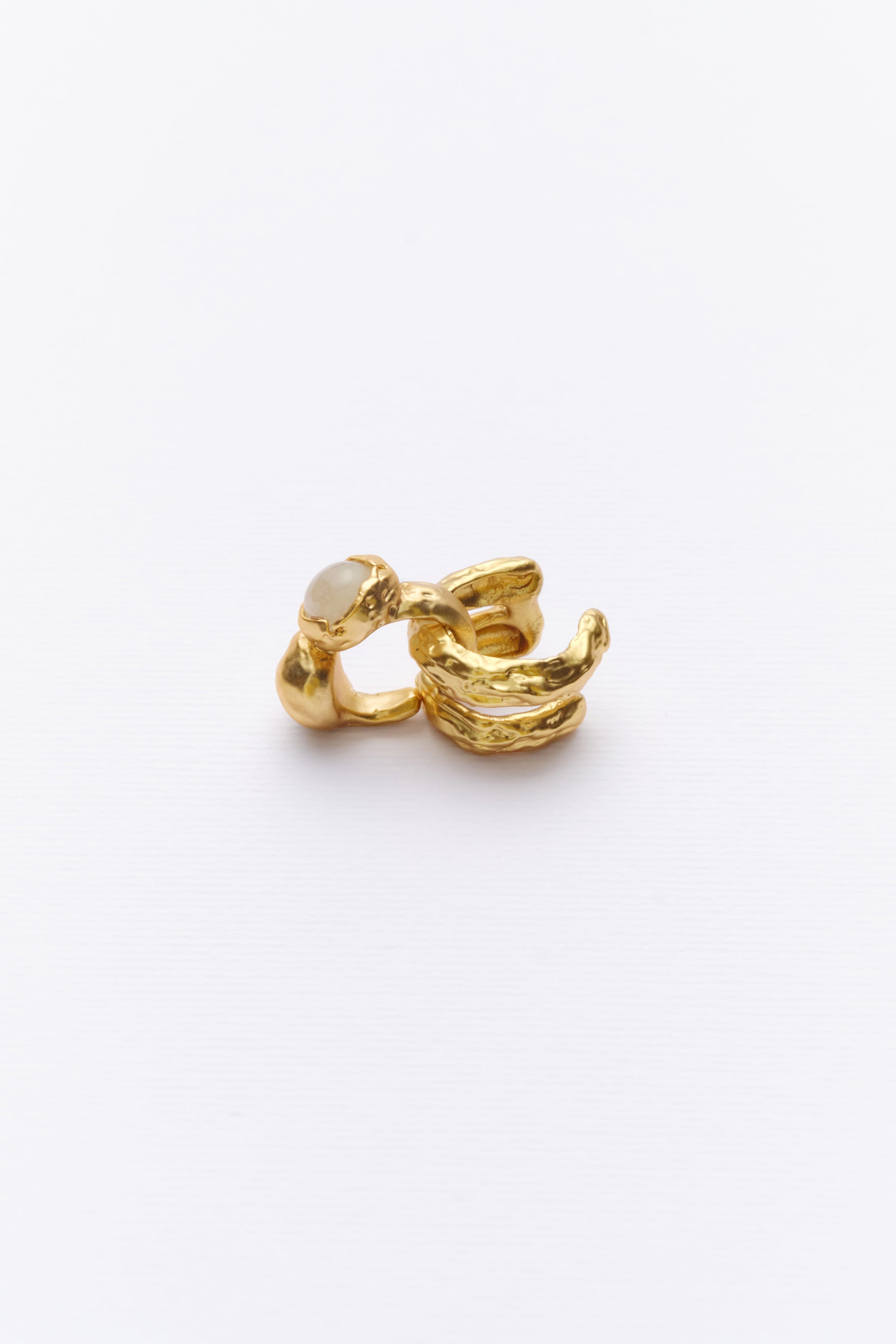 A gold-colored ear cuff with textured design, resembling sediment and stone layers, placed against a white background.