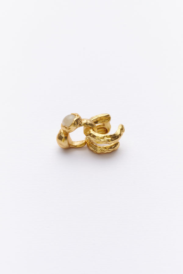 A gold-colored ear cuff with textured design, resembling sediment and stone layers, placed against a white background.