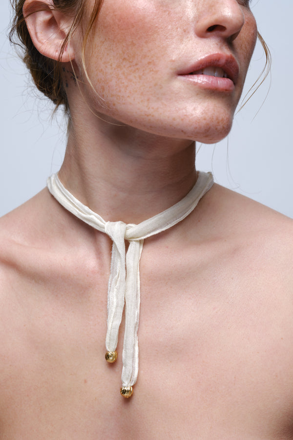 Gold textured shell pendant necklace with silk cord tied at neck worn on model