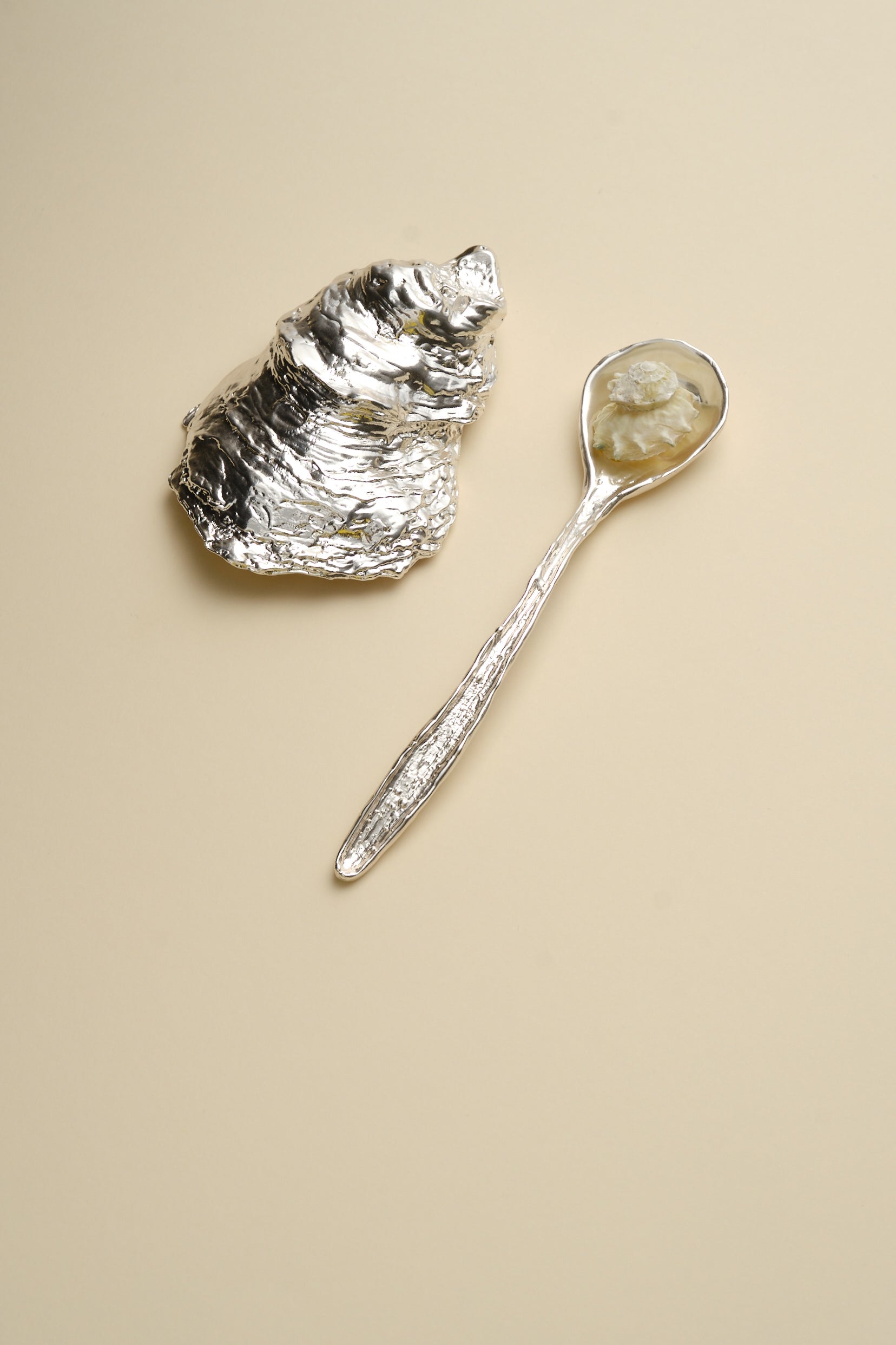 Silver sculptural oyster shell dish and spoon flat lay