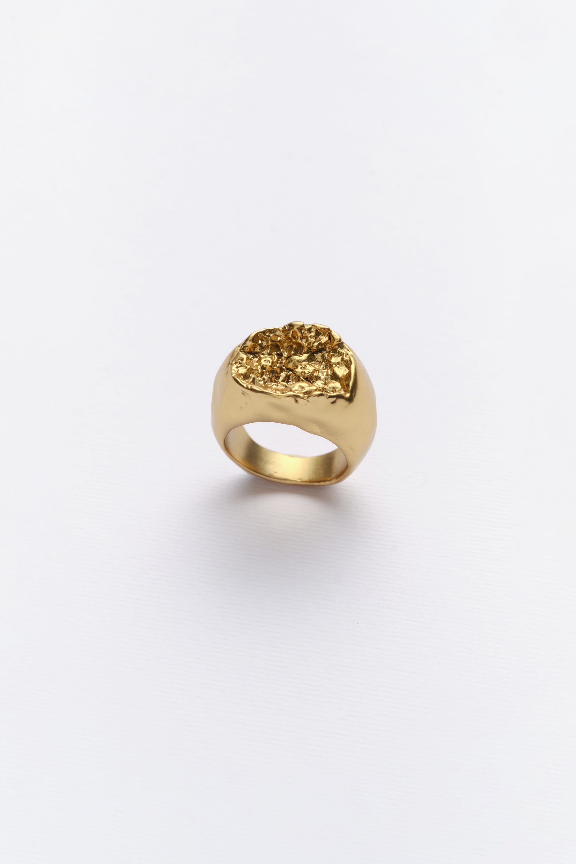 A gold-colored ring with an organic texture inspired by rock in nature, displayed against a white background