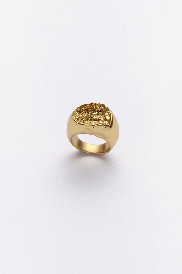 A gold-colored ring with an organic texture inspired by rock in nature, displayed against a white background