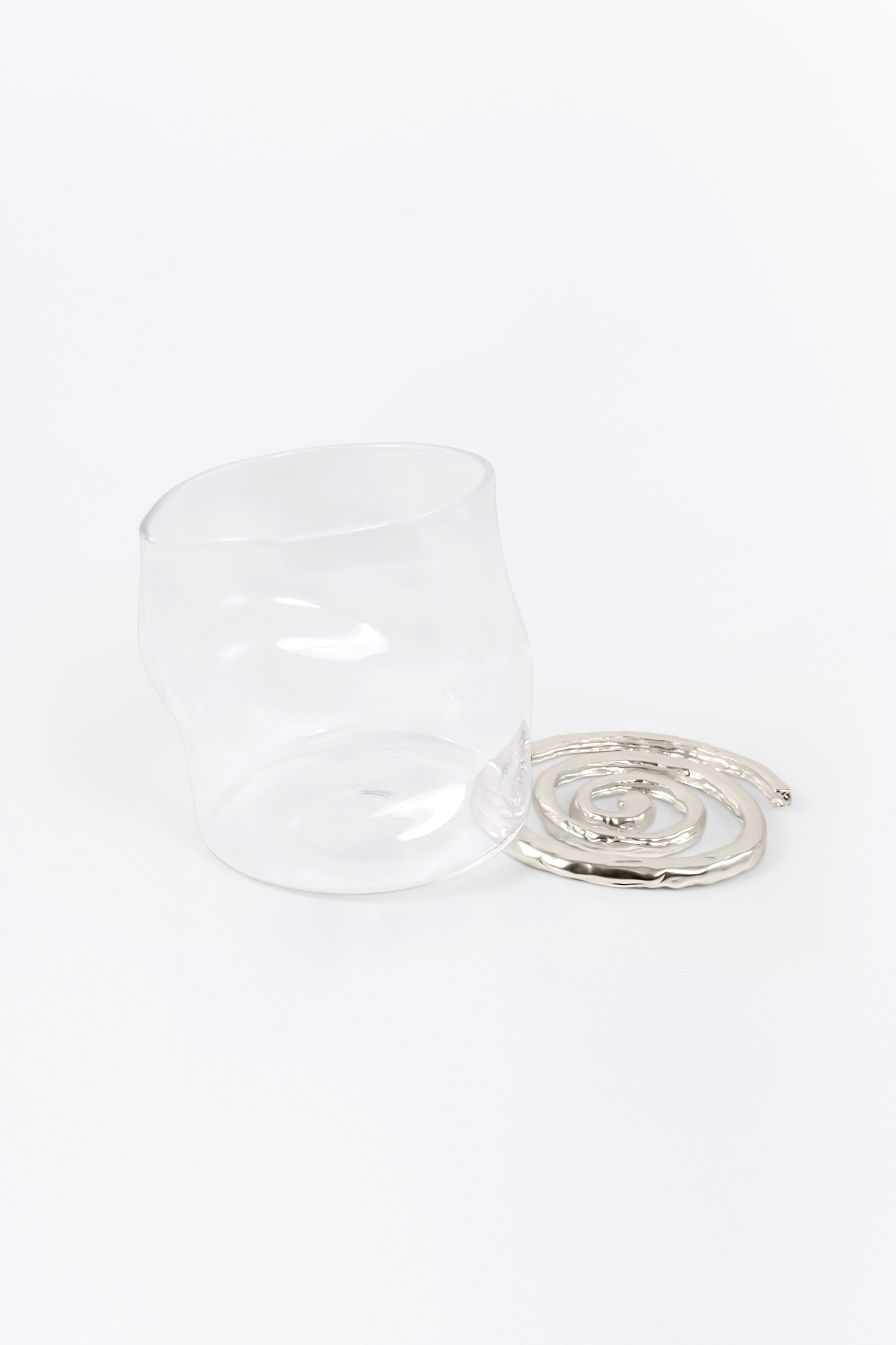 Clear glass cup with metallic spiral coaster on white background