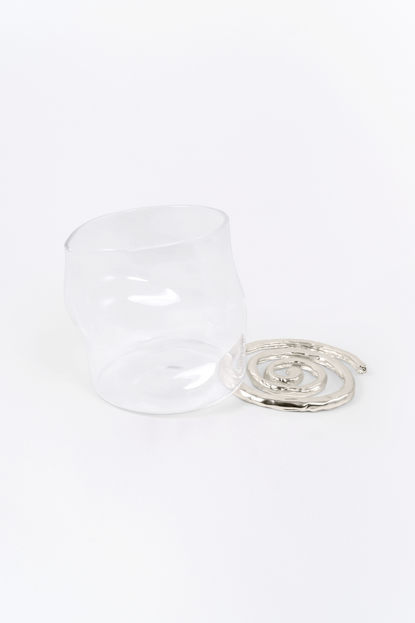 Clear glass cup with metallic spiral coaster on white background
