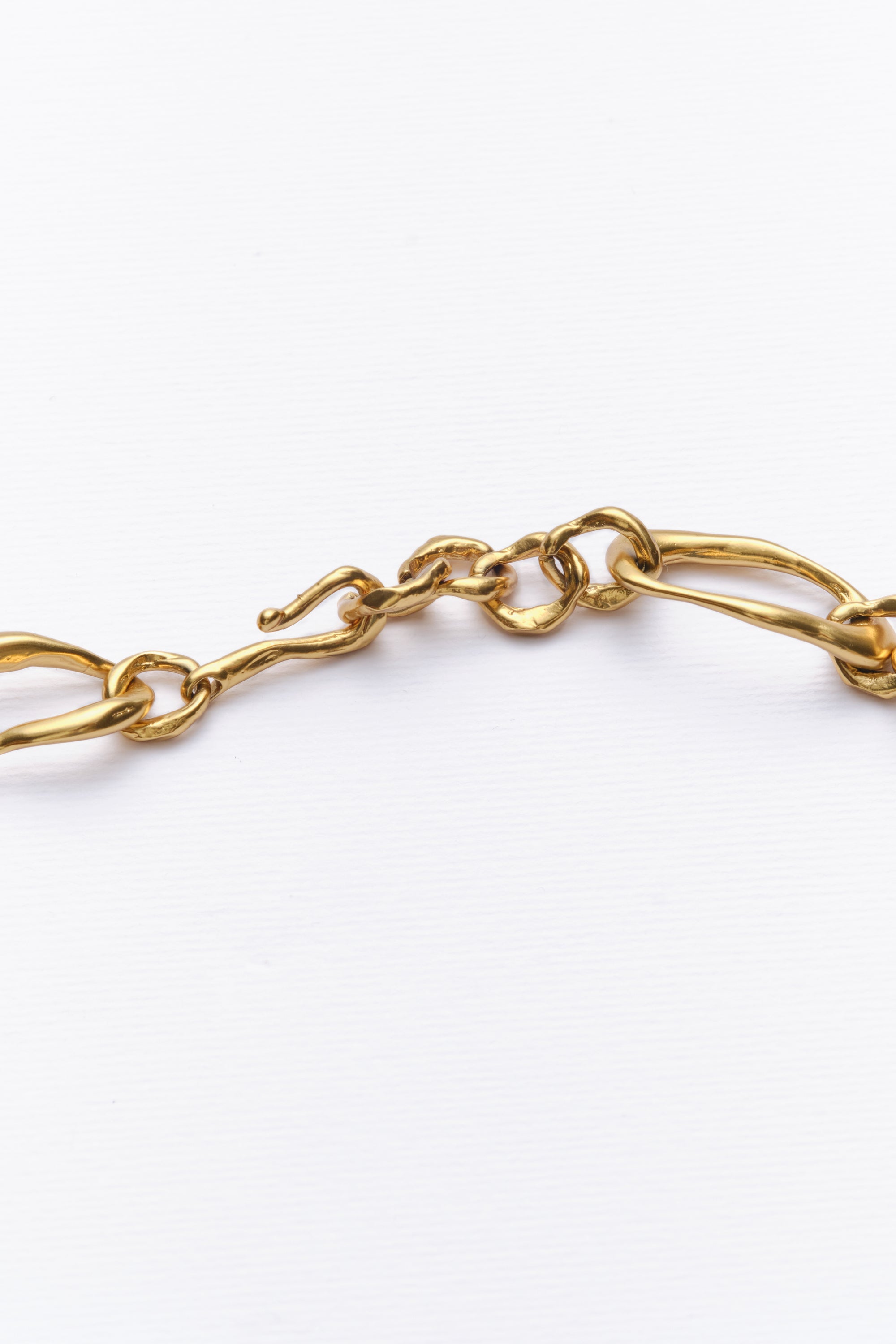Close-up of gold necklace clasp and textured chain links on white background