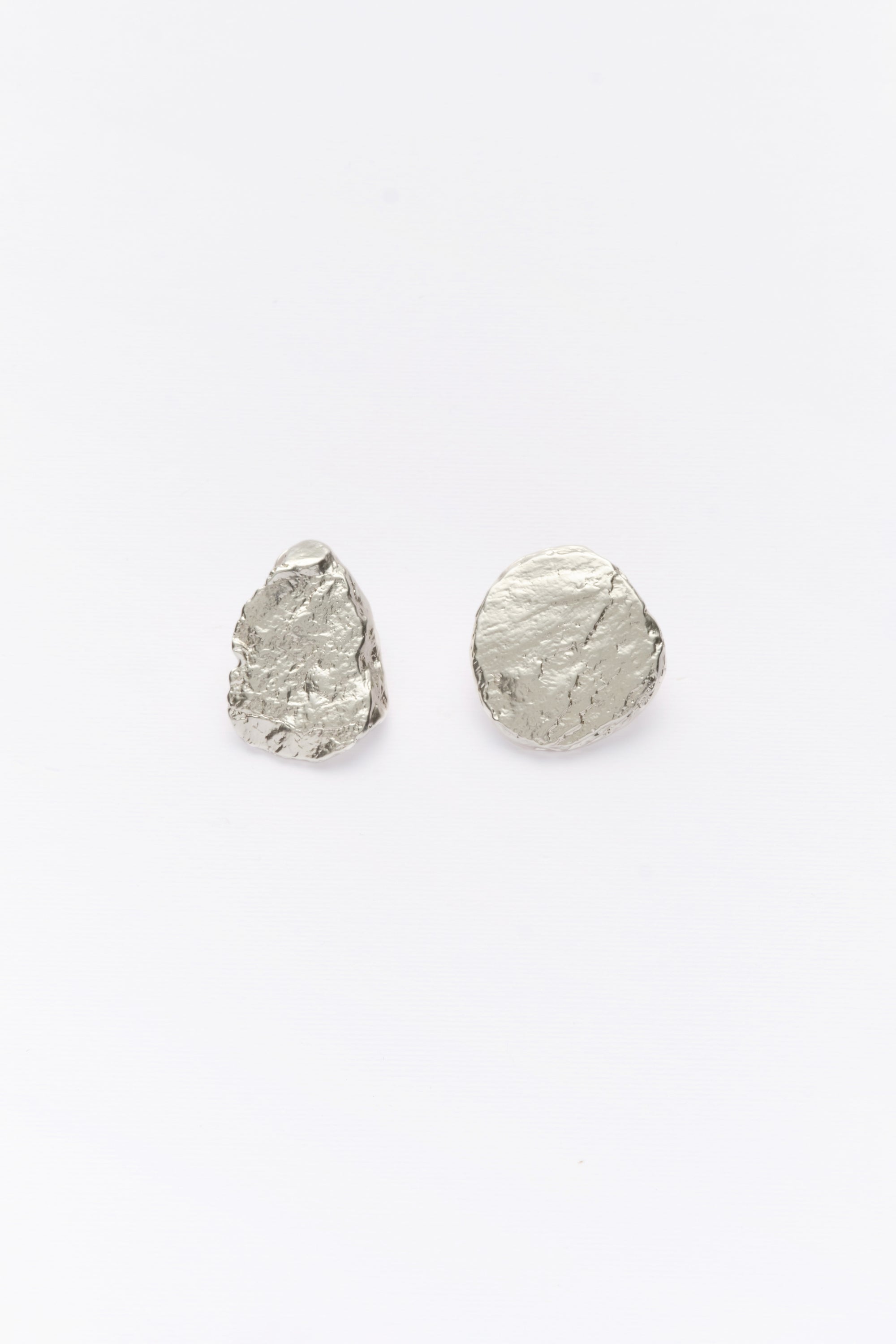 A pair of silver, asymmetric earrings with a textured surface on a white background.