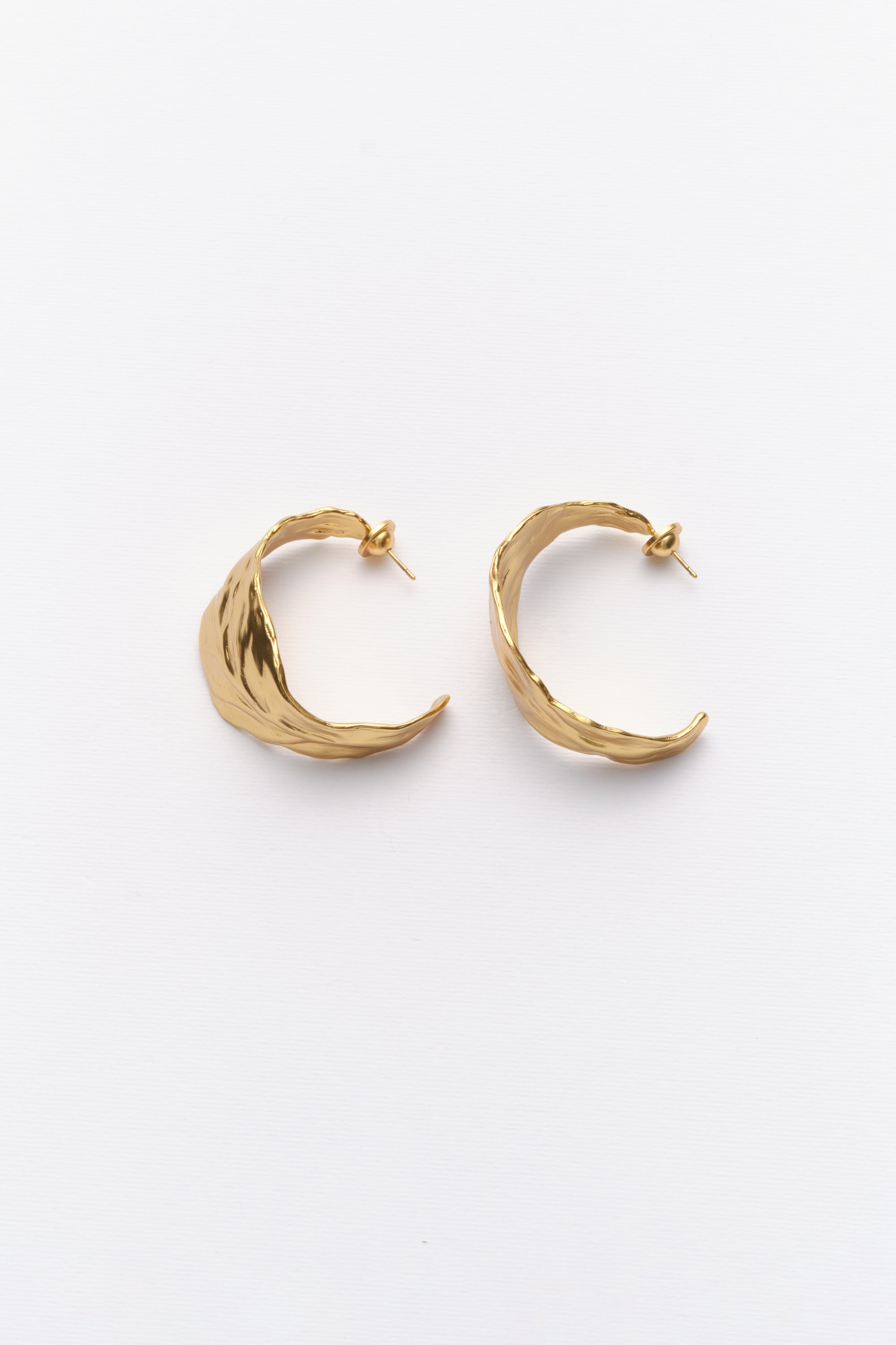A pair of gold-colored hoop earrings with a leaf texture on a white background.
