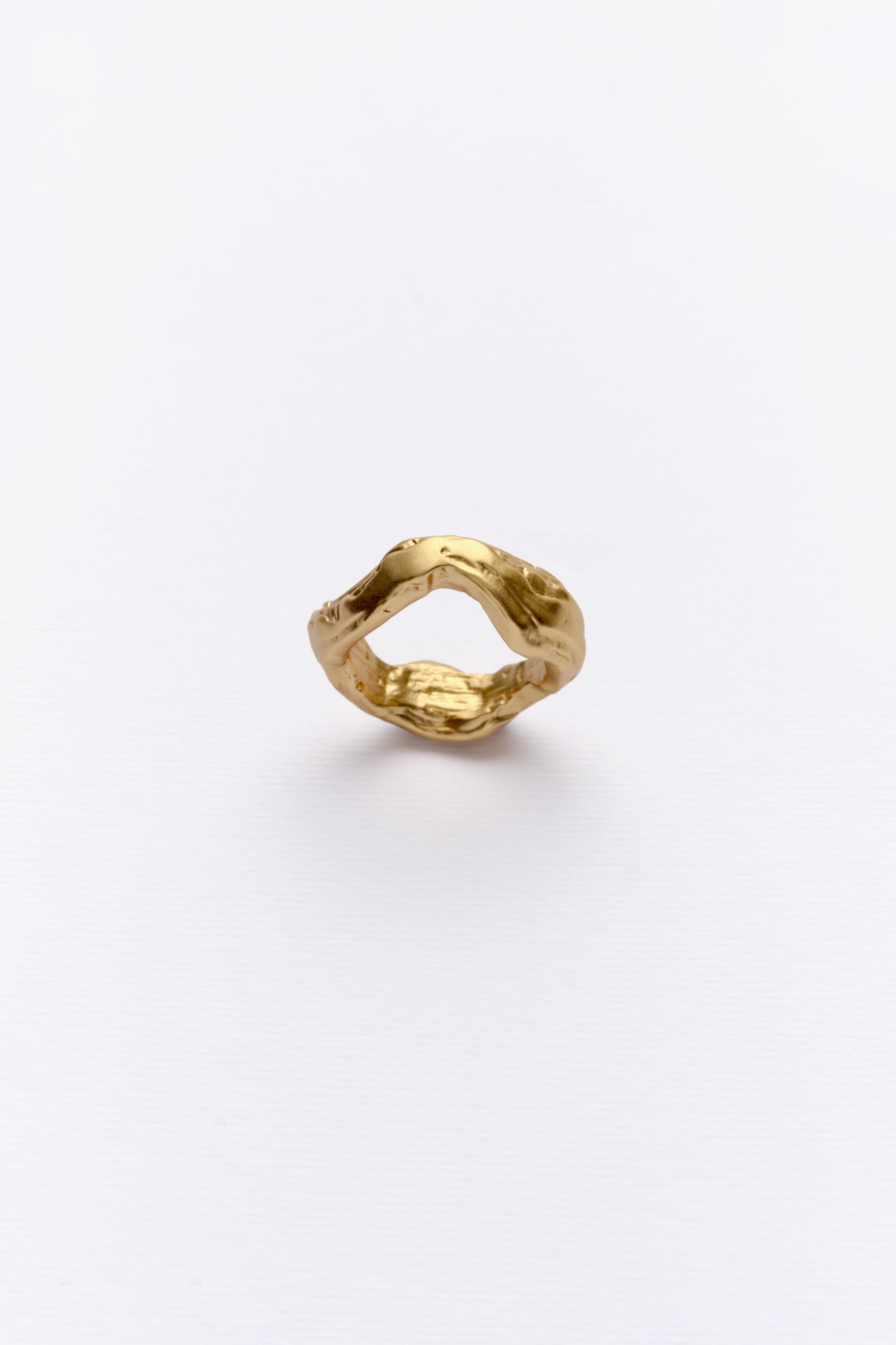 A gold-colored ring with a unique design, featuring a grooved, circular shape that resembles the appearance of soil layers and stone.