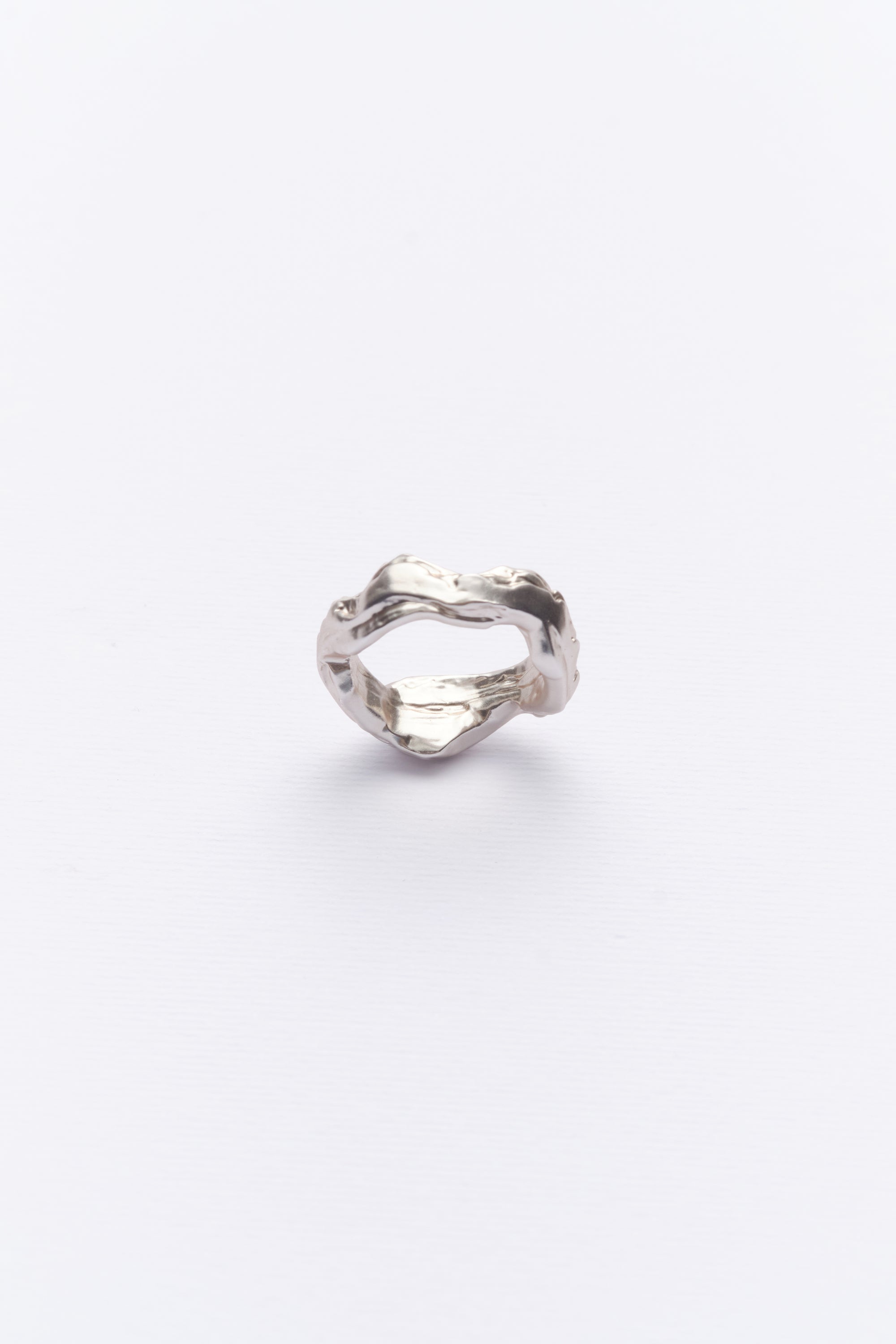 A silver ring with a textured design resembling soil layers and stone, displayed against a white background.