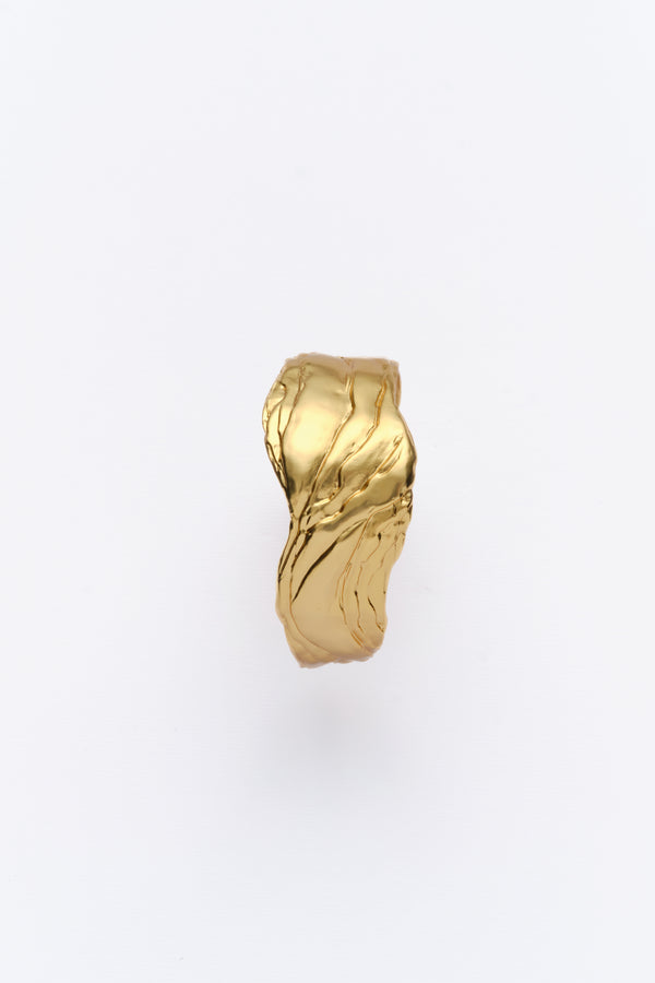 A gold-colored statement cuff bracelet with textured surfaces, displayed against a white background.
