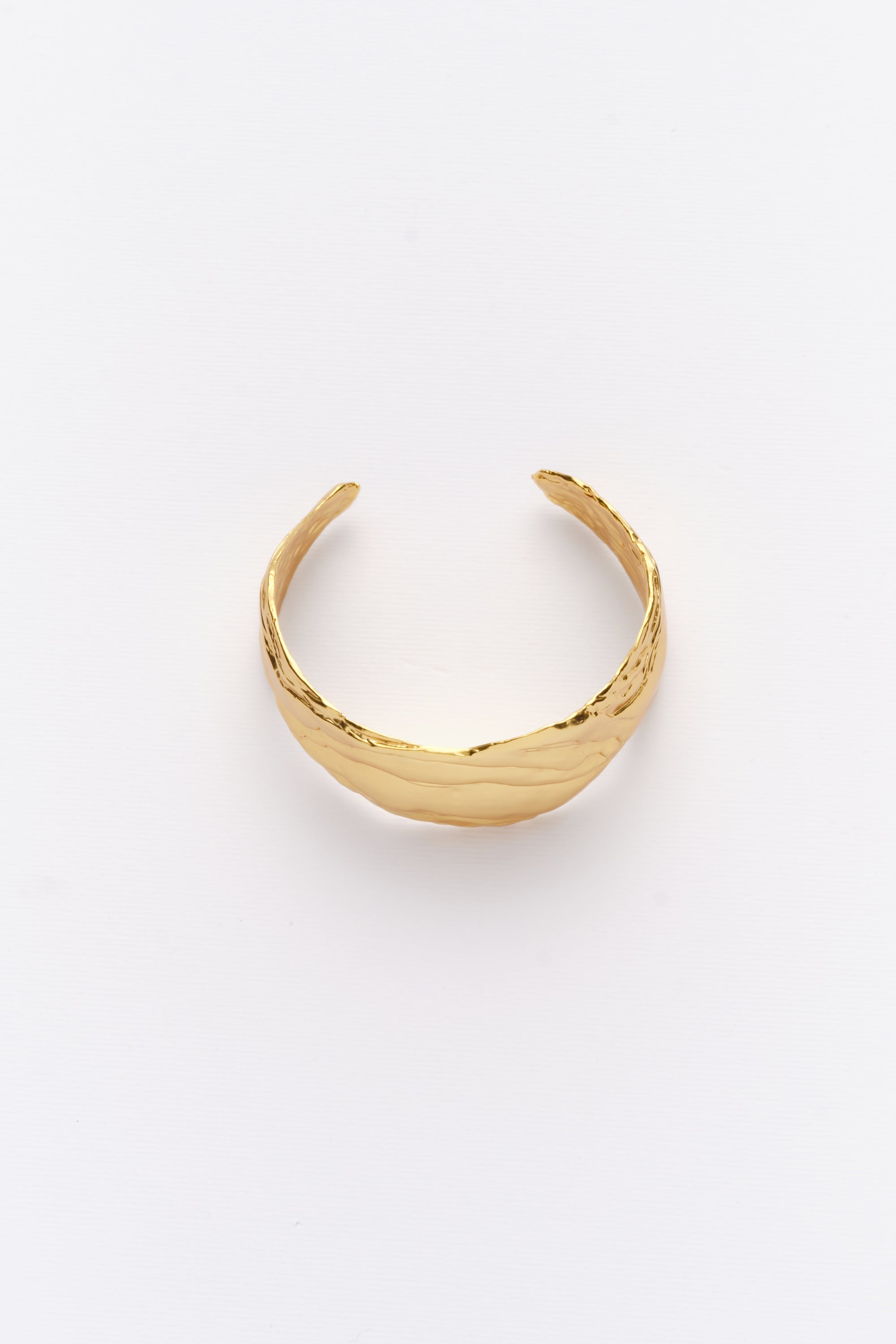 A gold-colored statement cuff bracelet with textured surfaces, displayed against a white background.
