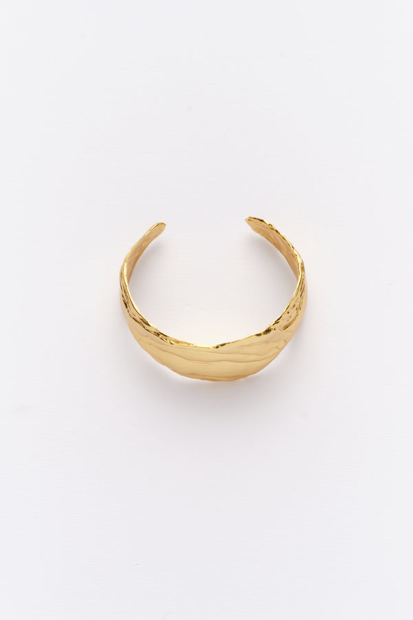 A gold-colored statement cuff bracelet with textured surfaces, displayed against a white background.