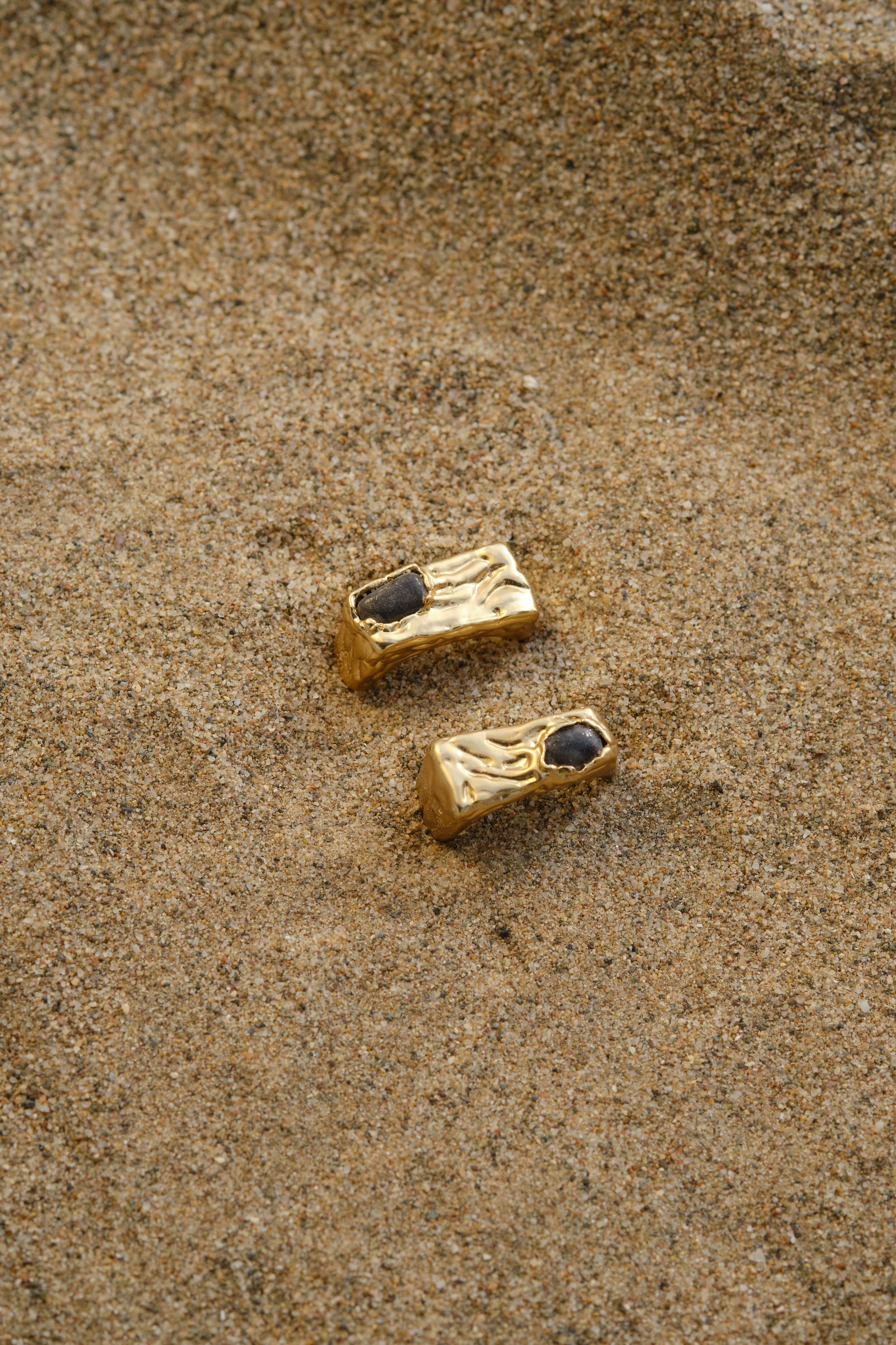 Gold textured signet rings styled on sand