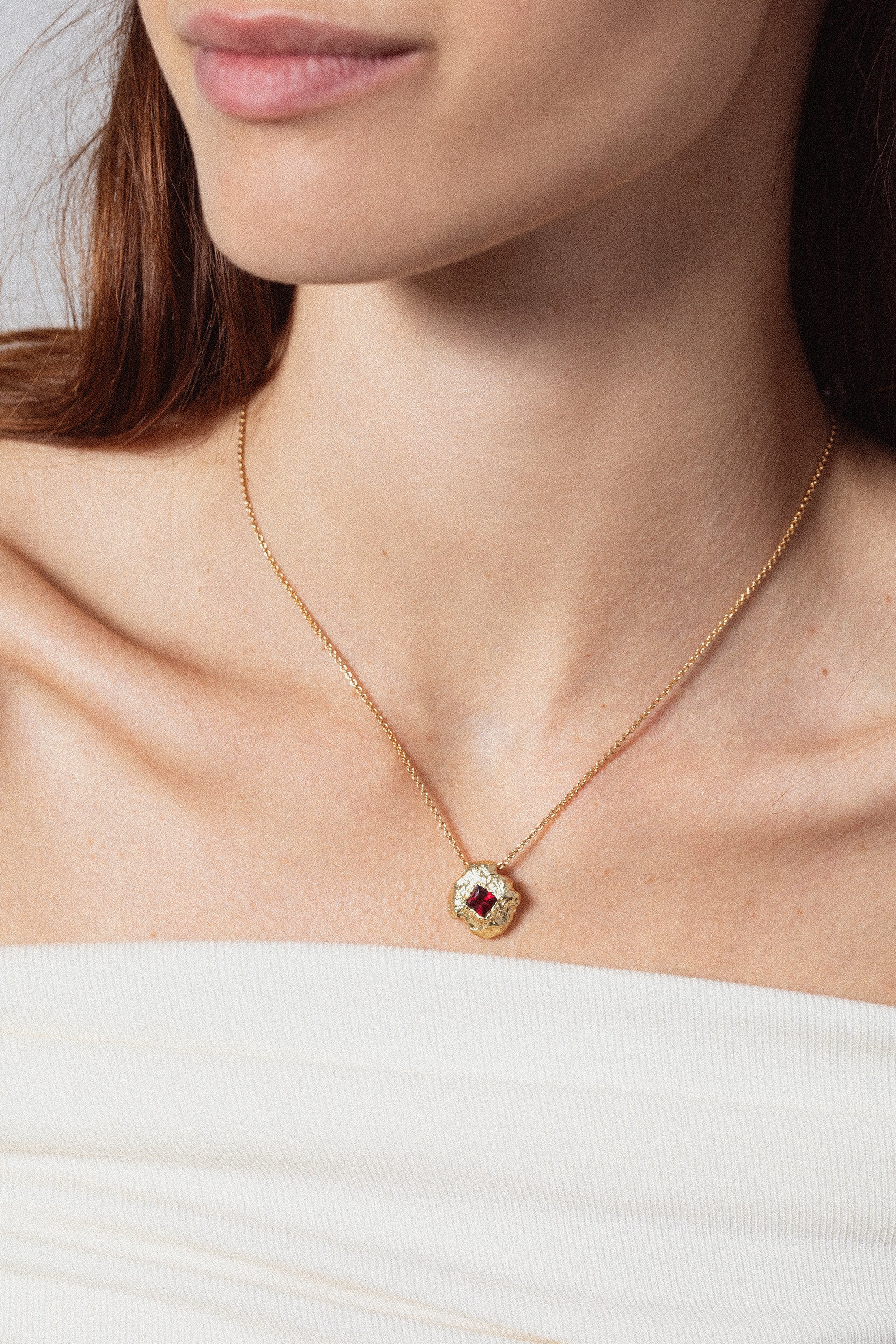 Gold textured round pendant necklace with red gemstone worn on model