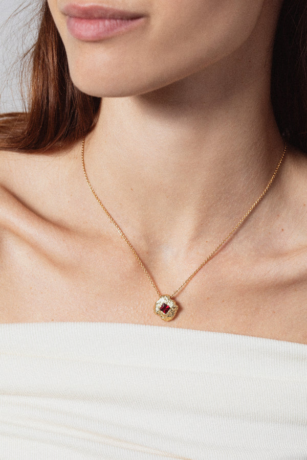 Gold textured round pendant necklace with red gemstone worn on model