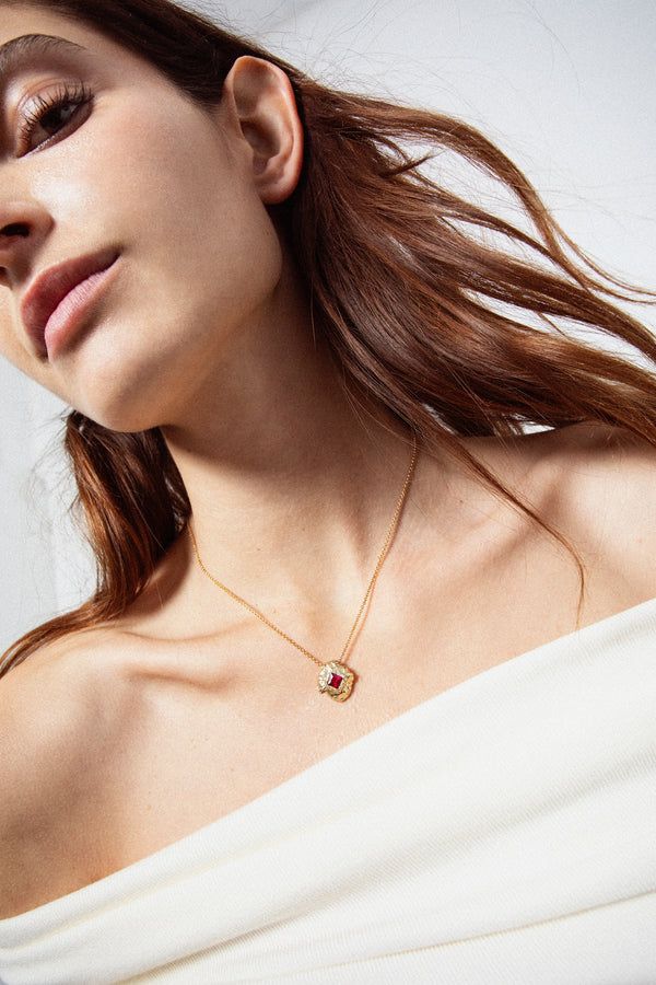 Gold textured round pendant necklace with red gemstone on model portrait
