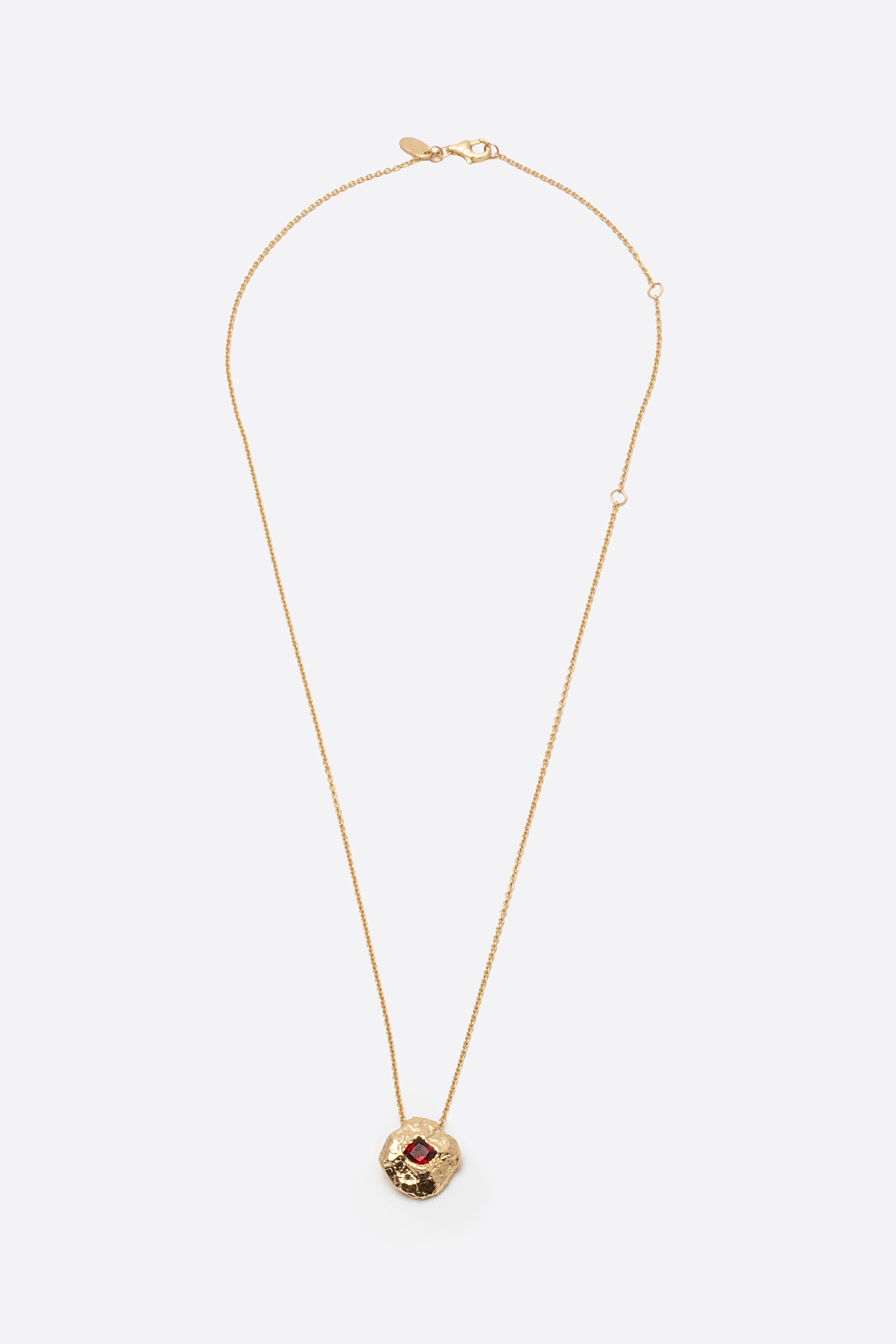 Gold textured round pendant necklace with square red gemstone flat lay