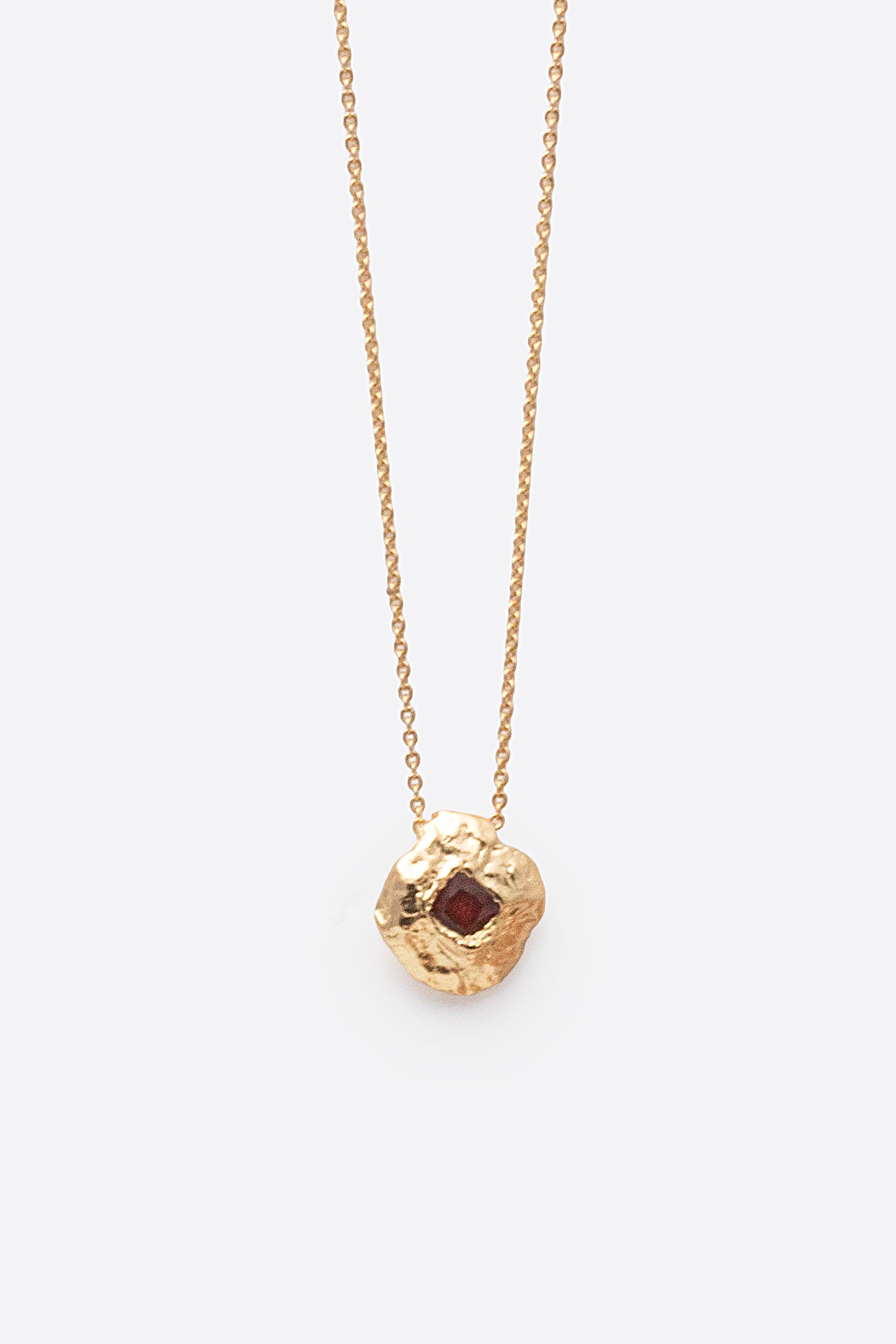 Close-up of gold textured round pendant necklace with square red gemstone