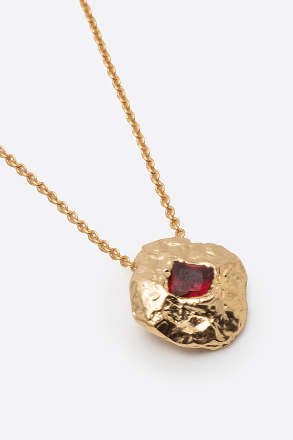 Detail of gold textured round pendant with square red gemstone