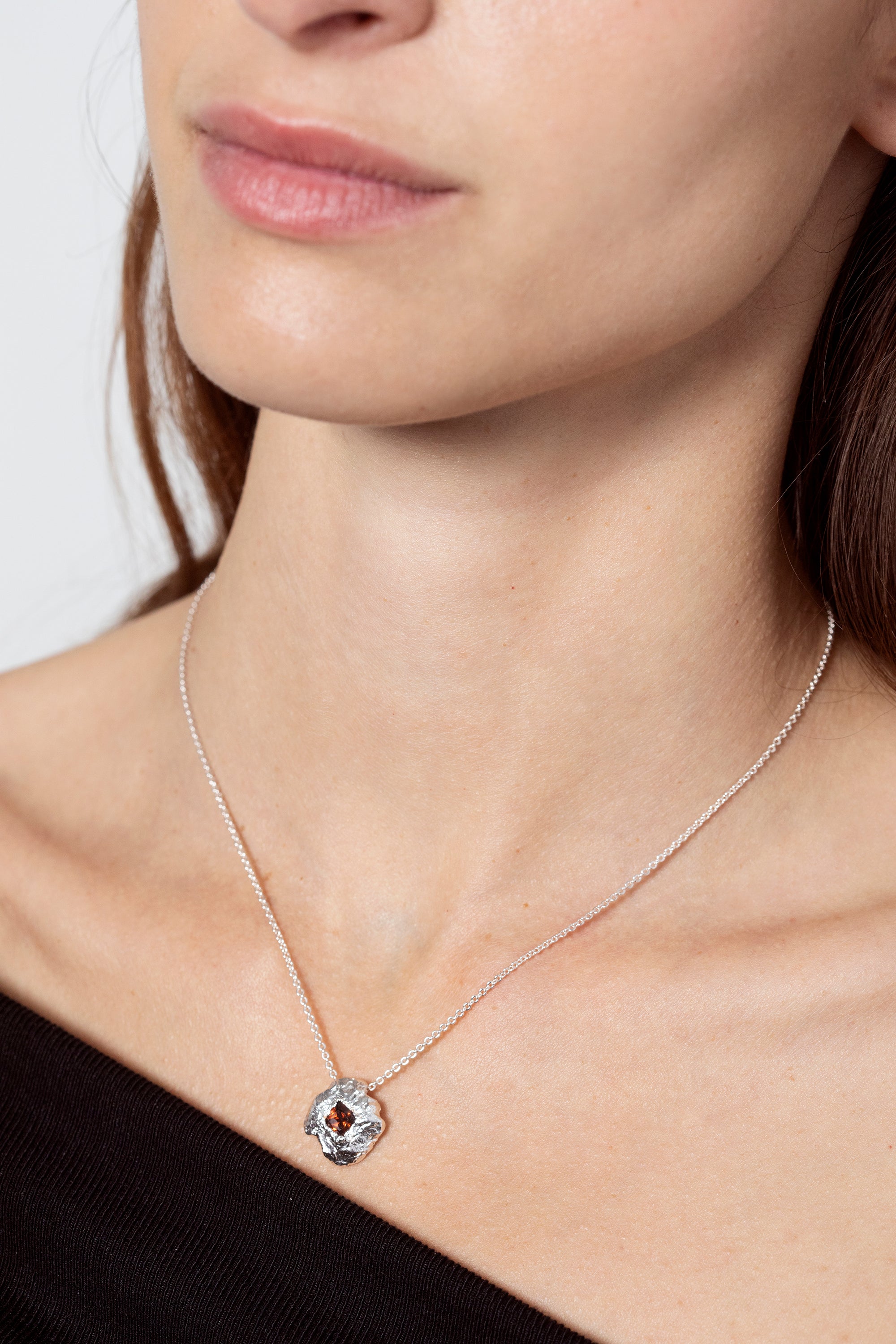 Silver textured round pendant necklace with red gemstone worn on model